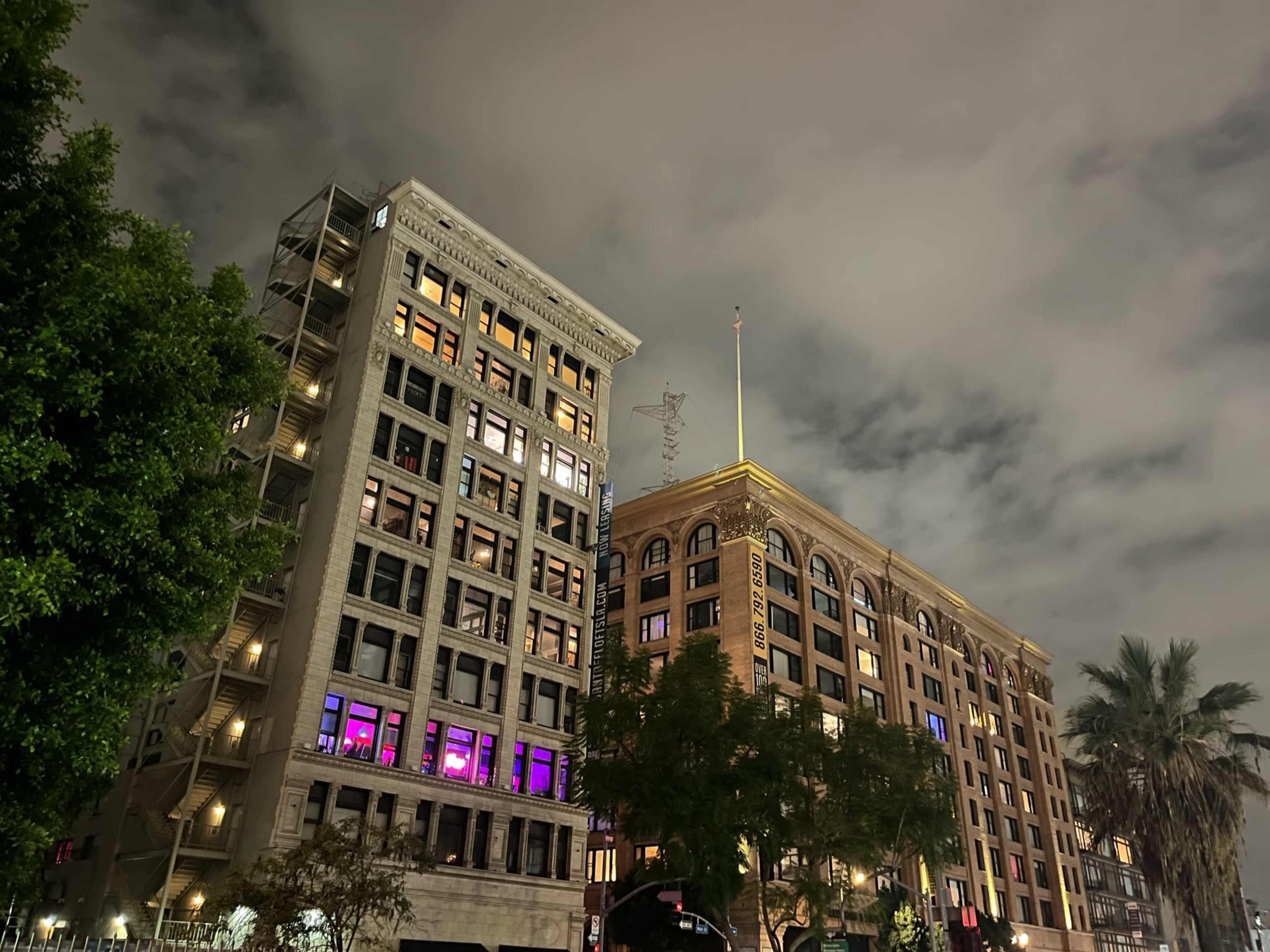 A view of two historic brick buildings lit at night, with clouds overhead and trees in the foreground.