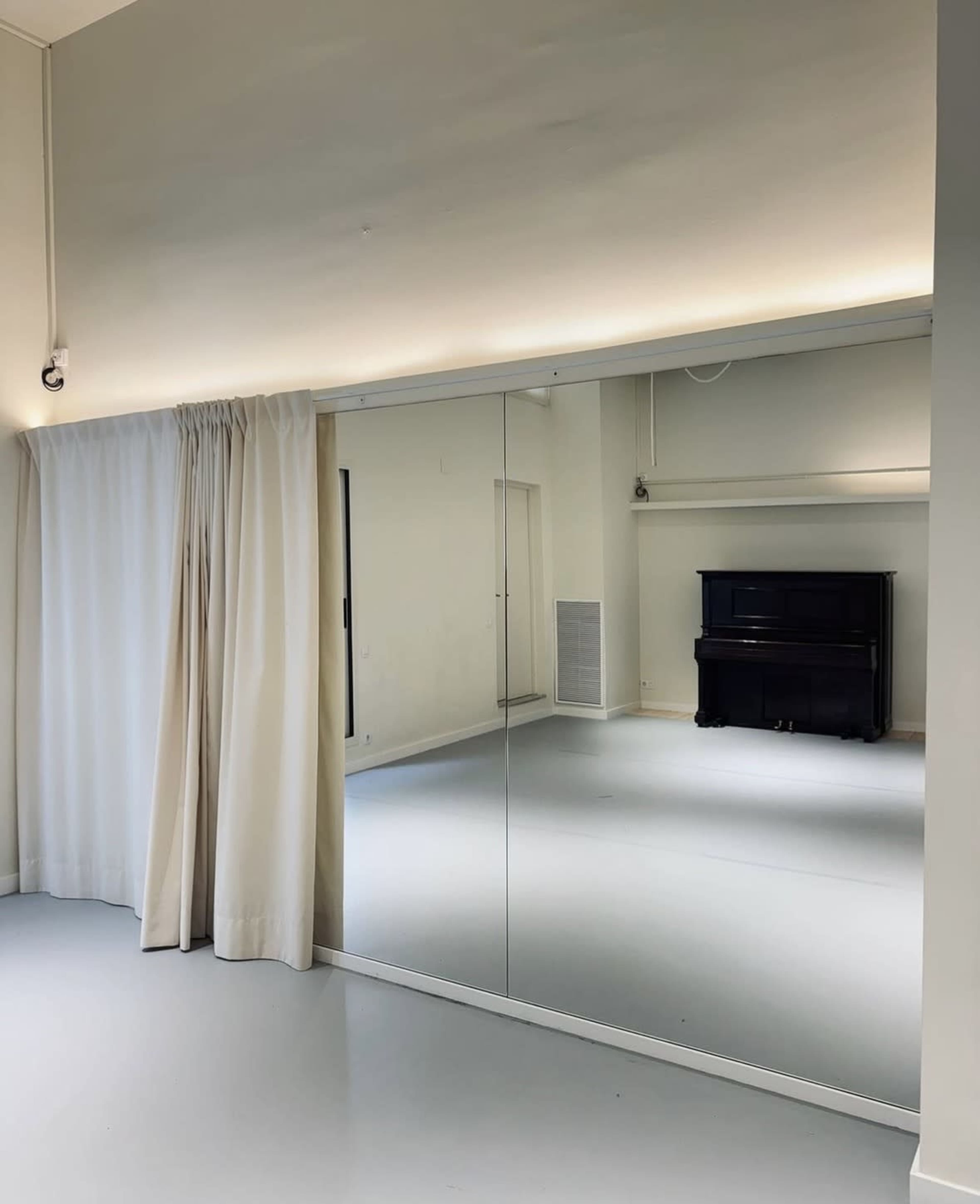 The image shows a bright room with a piano in the corner, large mirrors on one wall, and a curtain partially drawn.