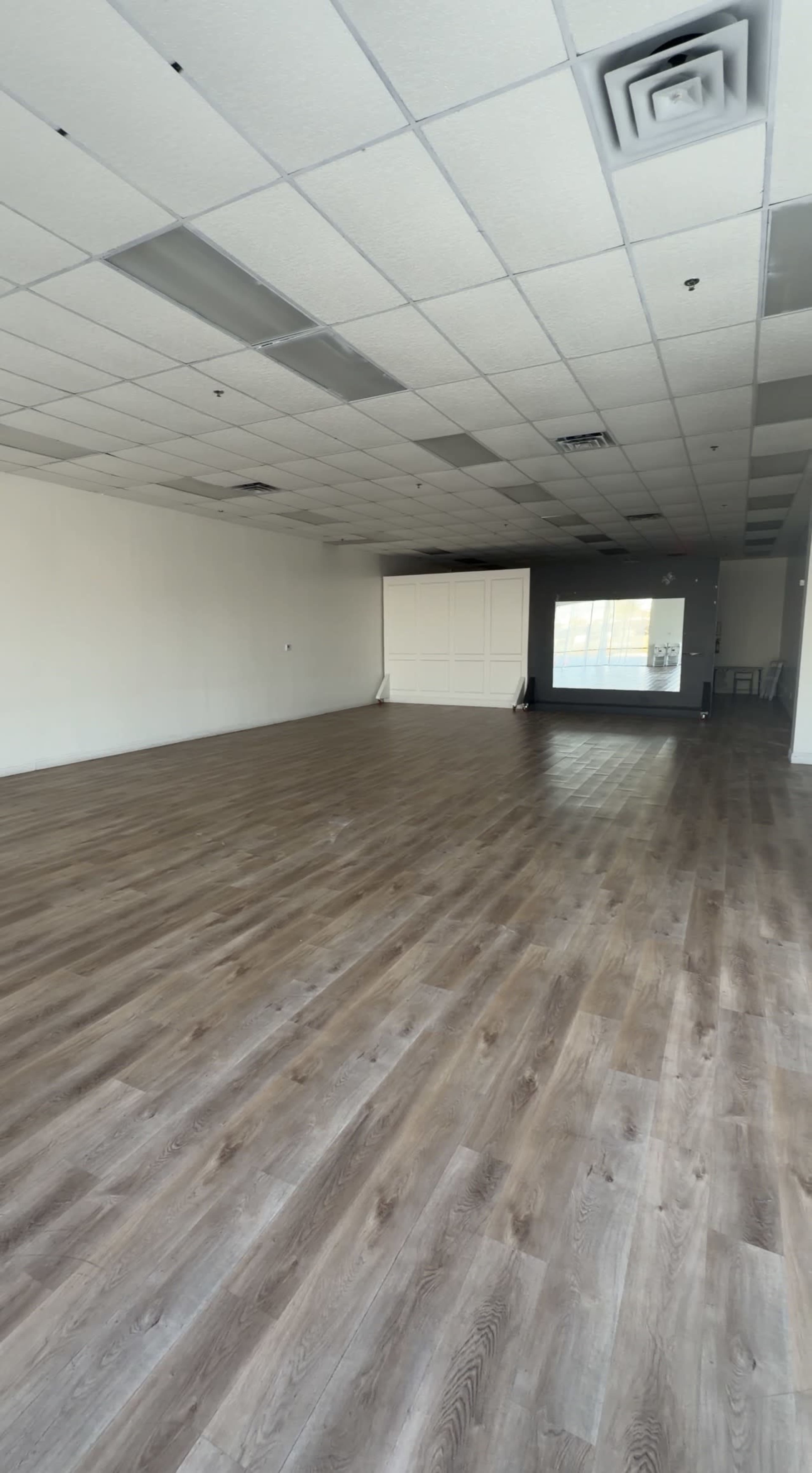 The image shows a spacious, empty retail room with wooden laminate flooring and white walls.