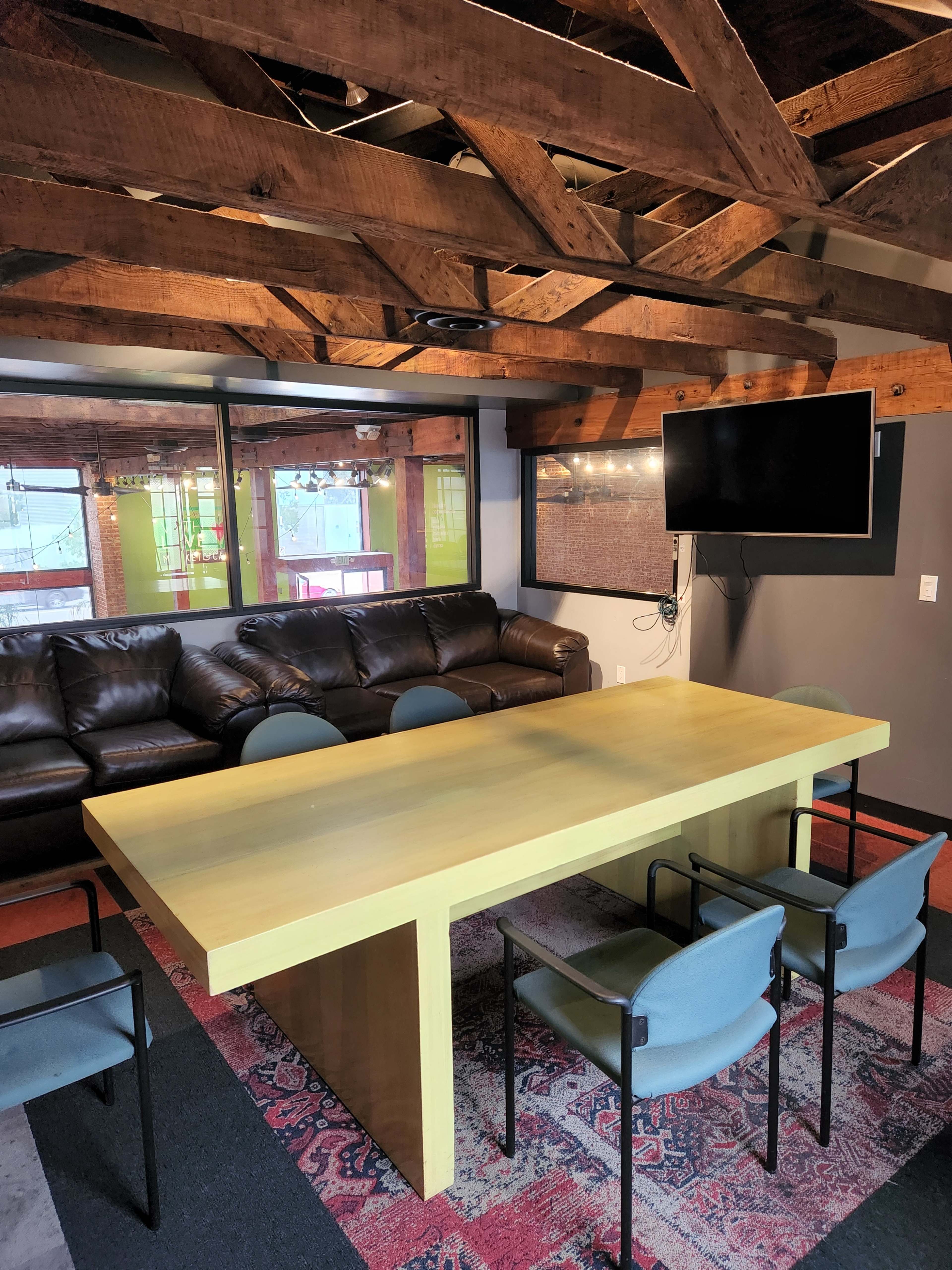 A meeting room with a large yellow table surrounded by black chairs, a leather couch, and exposed wooden beams above.