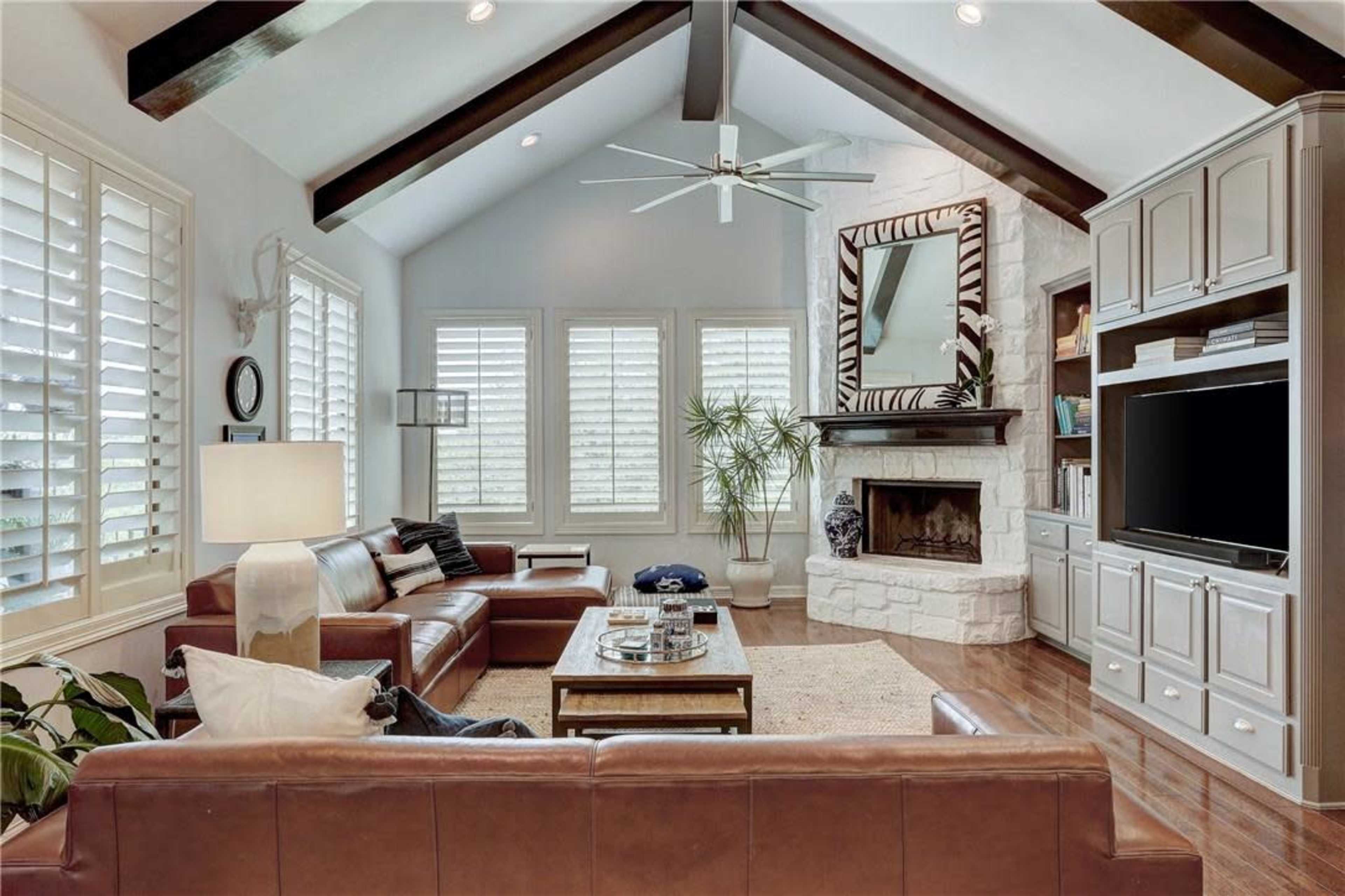 The living room features a high ceiling with exposed beams, a large fireplace, and contemporary furniture arranged around a central coffee table.