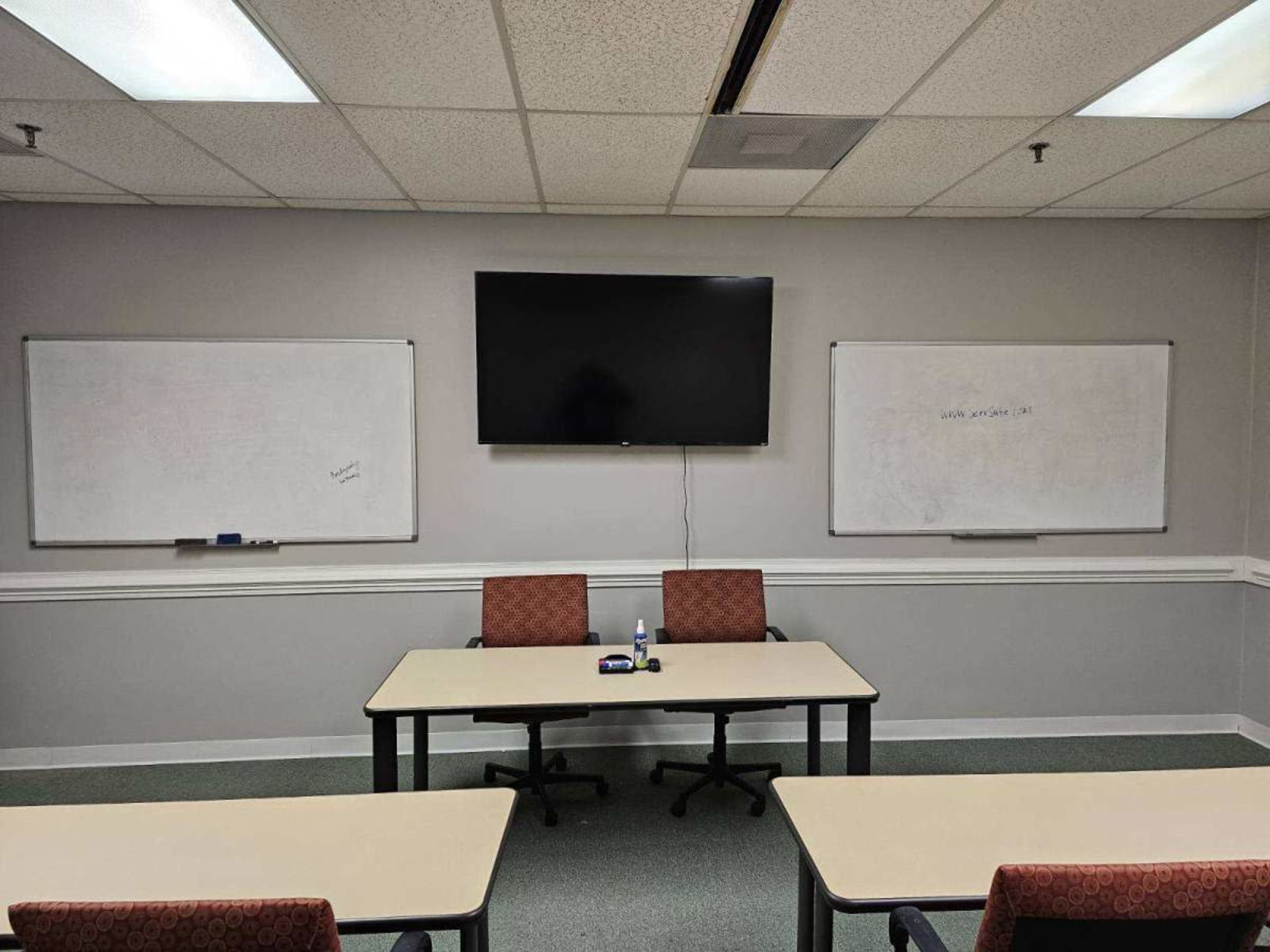 A meeting room features two whiteboards, a large TV screen, and a central table with two chairs.