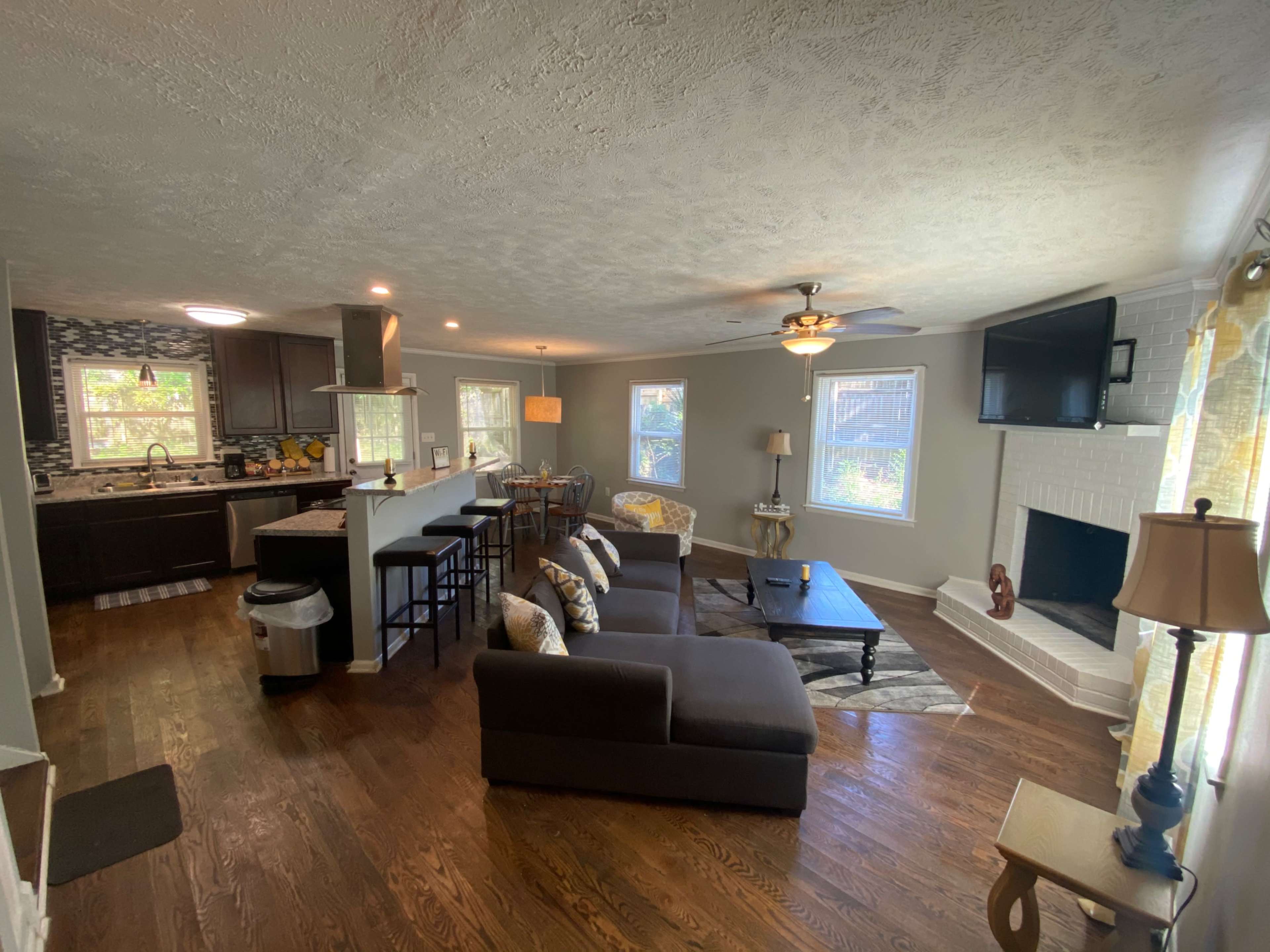 A modern living area with a dark sectional sofa, a dining space, and a kitchen visible in the background.