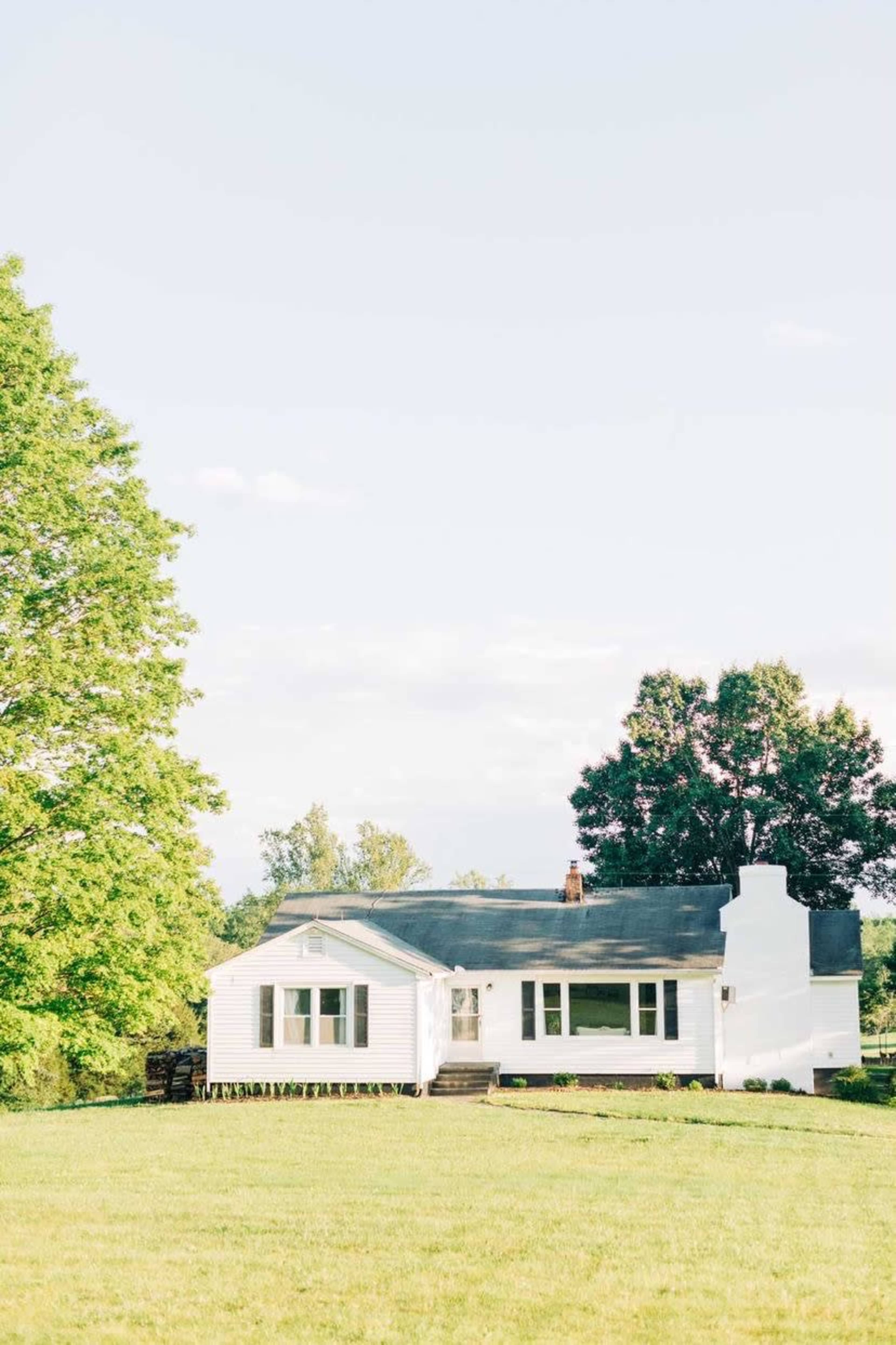 A white house sits on a grassy hill with trees in the background under a clear sky.
