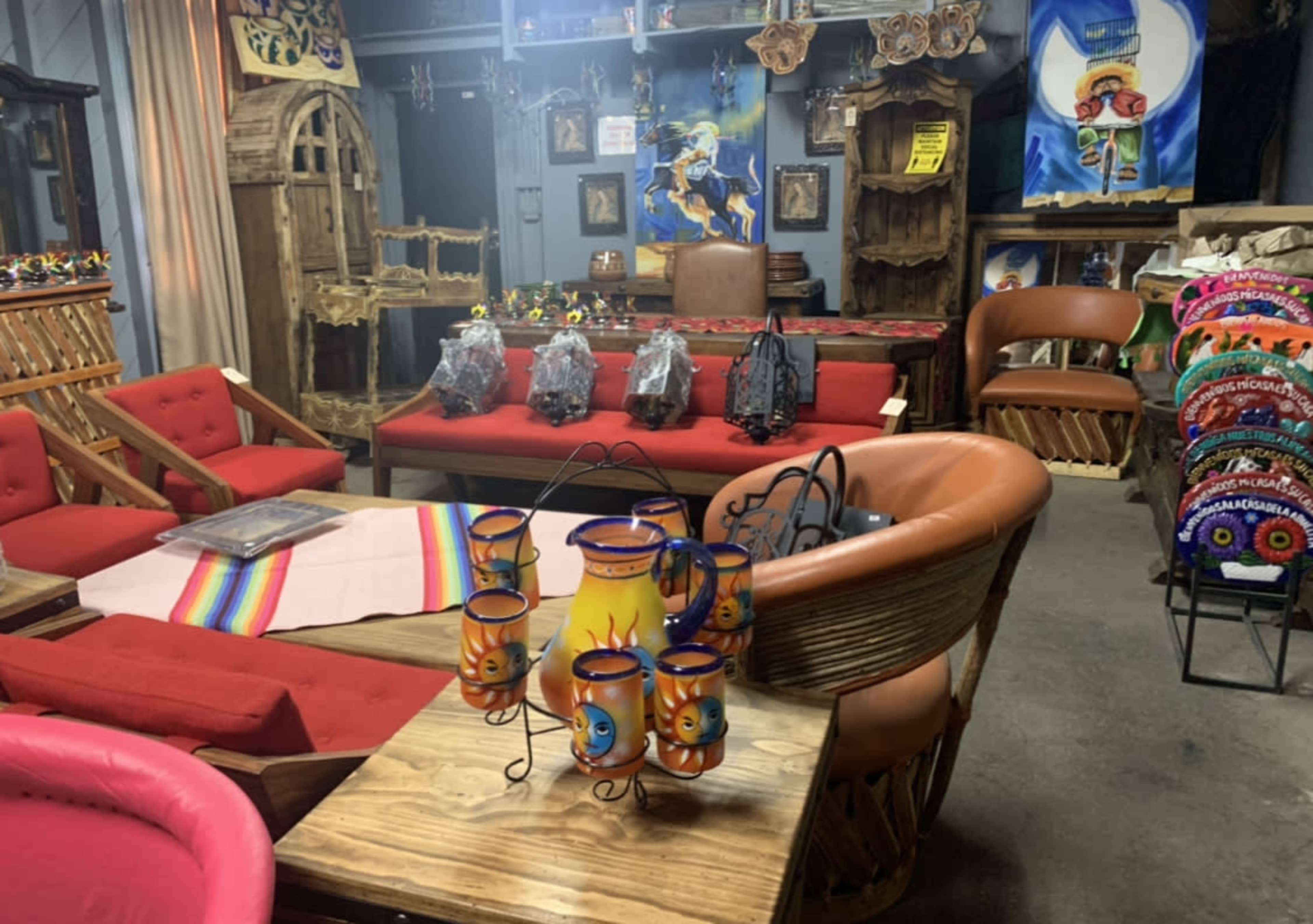 The image shows a colorful interior space featuring various wooden furniture pieces, decorative items, and woven textiles, with a focus on a table displaying a set of ceramic candle holders.