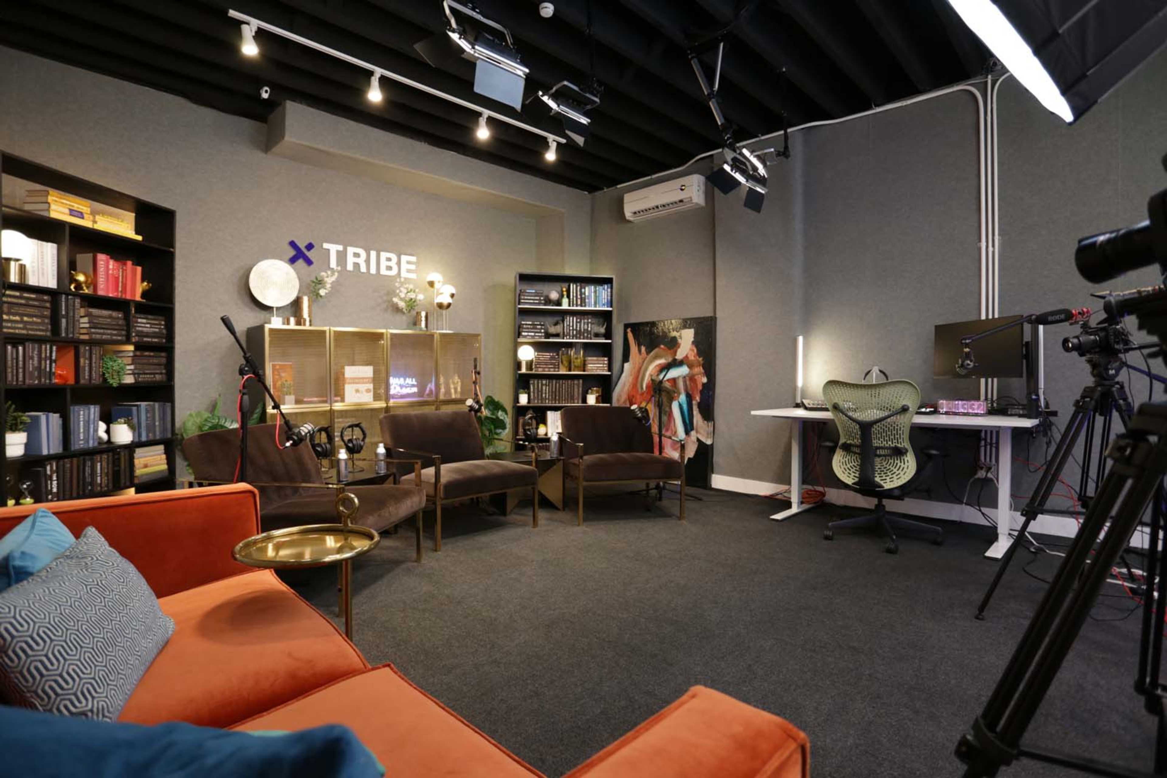 A modern studio setting with comfortable seating, bookshelves, and video equipment arranged for a podcast or interview.