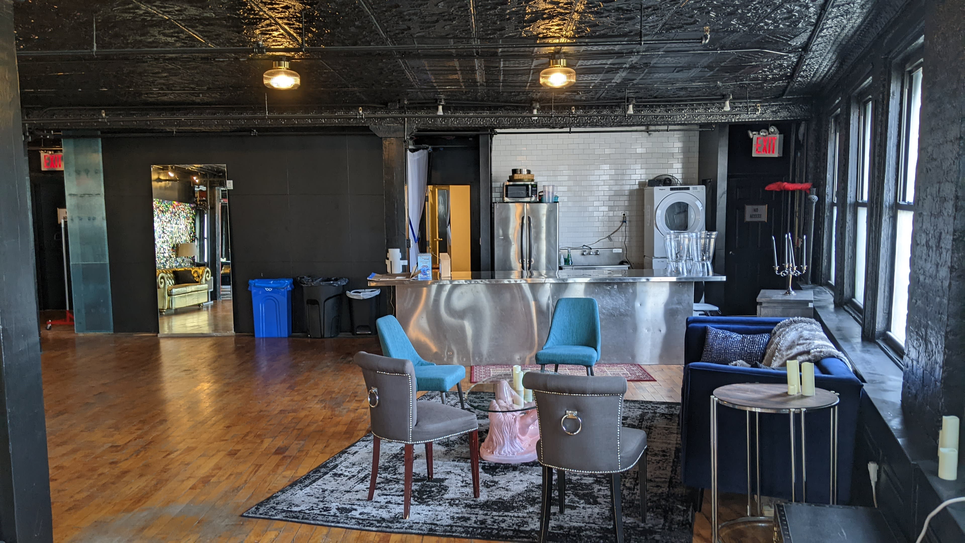 A spacious room with a bar area, seating arrangements including chairs and sofas, and large windows allowing natural light.