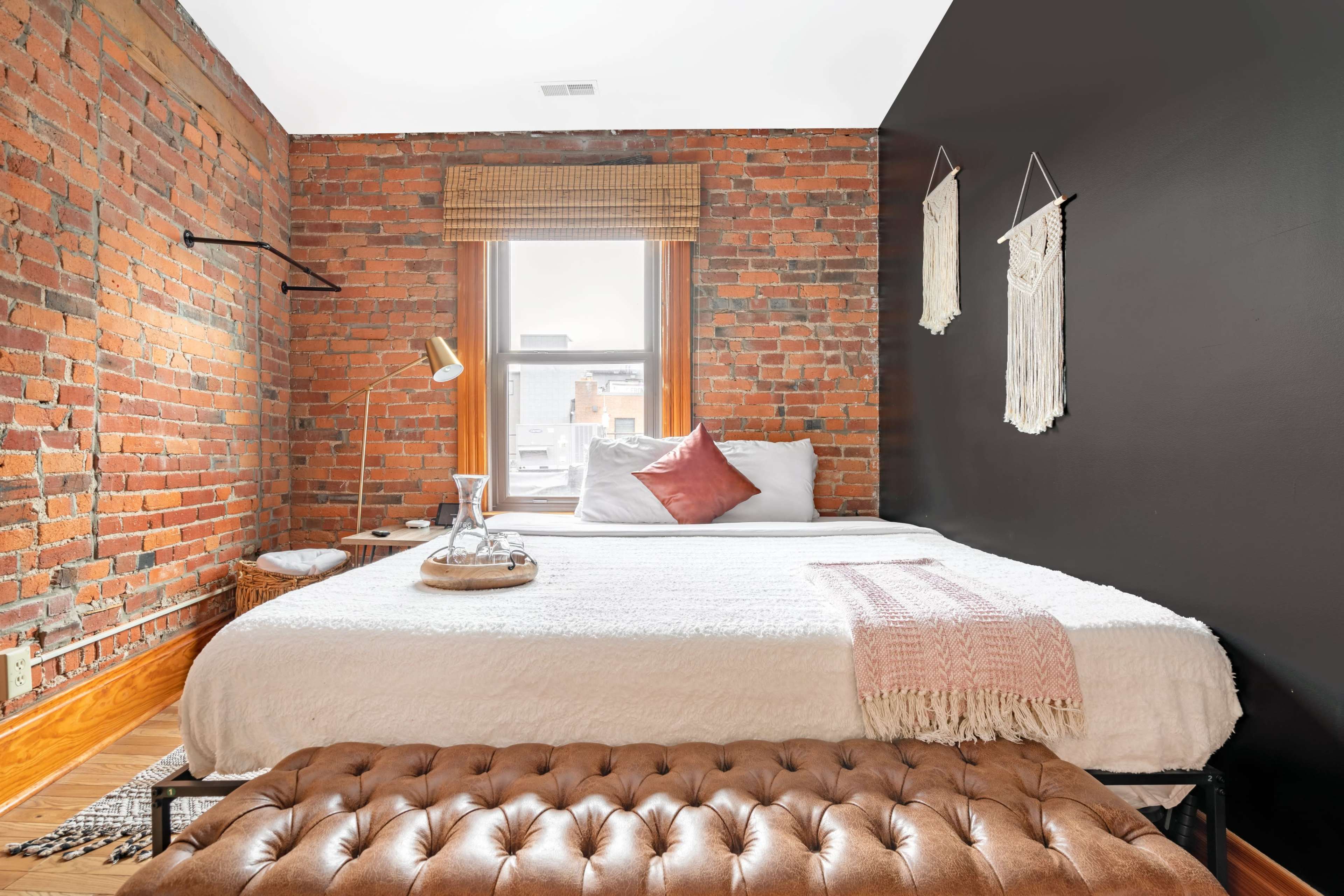 A modern bedroom with exposed brick walls, a large bed with white bedding, and a decorative bench at the foot of the bed.