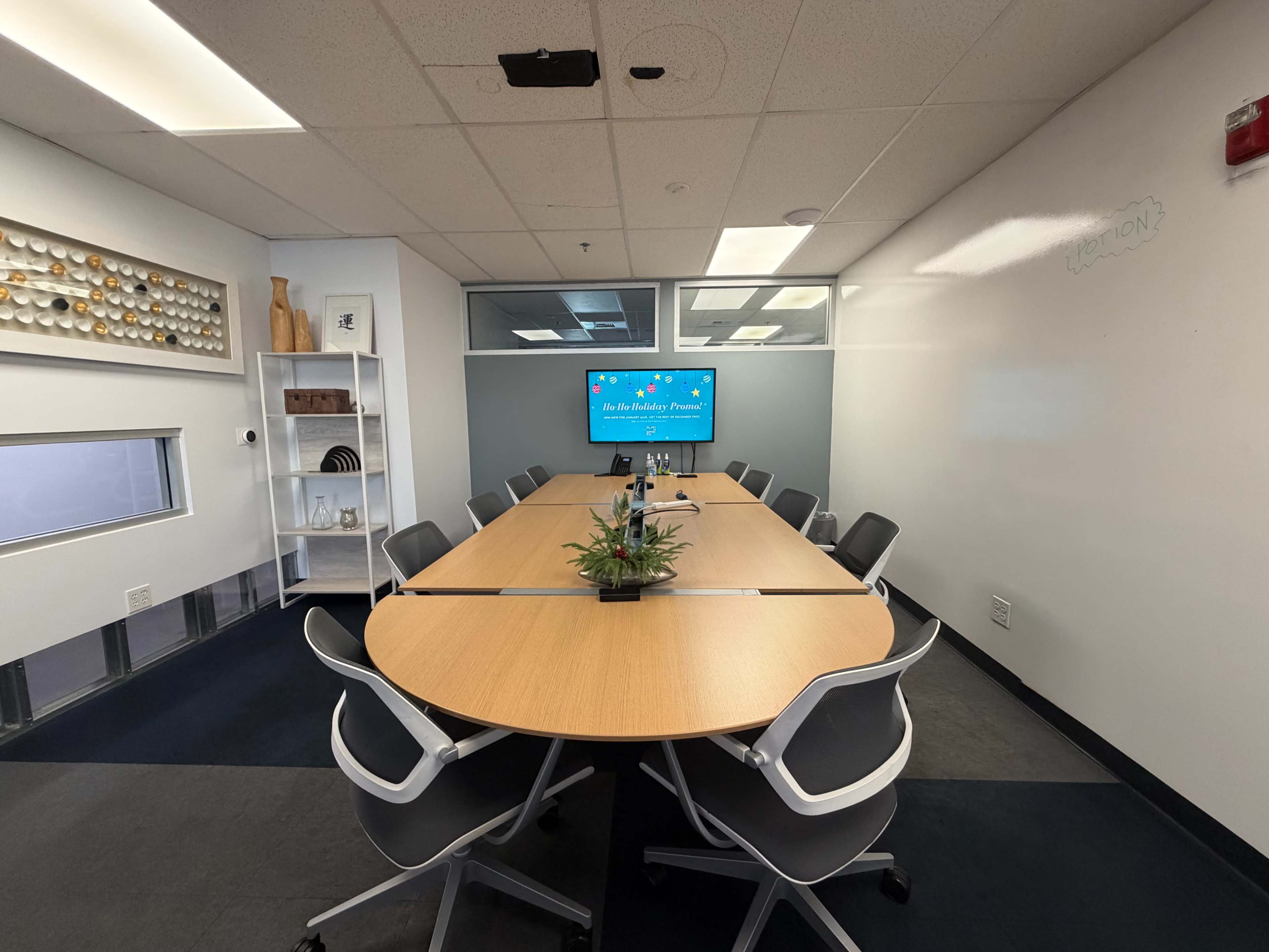 A modern conference room features a large oval table surrounded by ergonomic chairs, with a screen displaying a presentation on one wall.