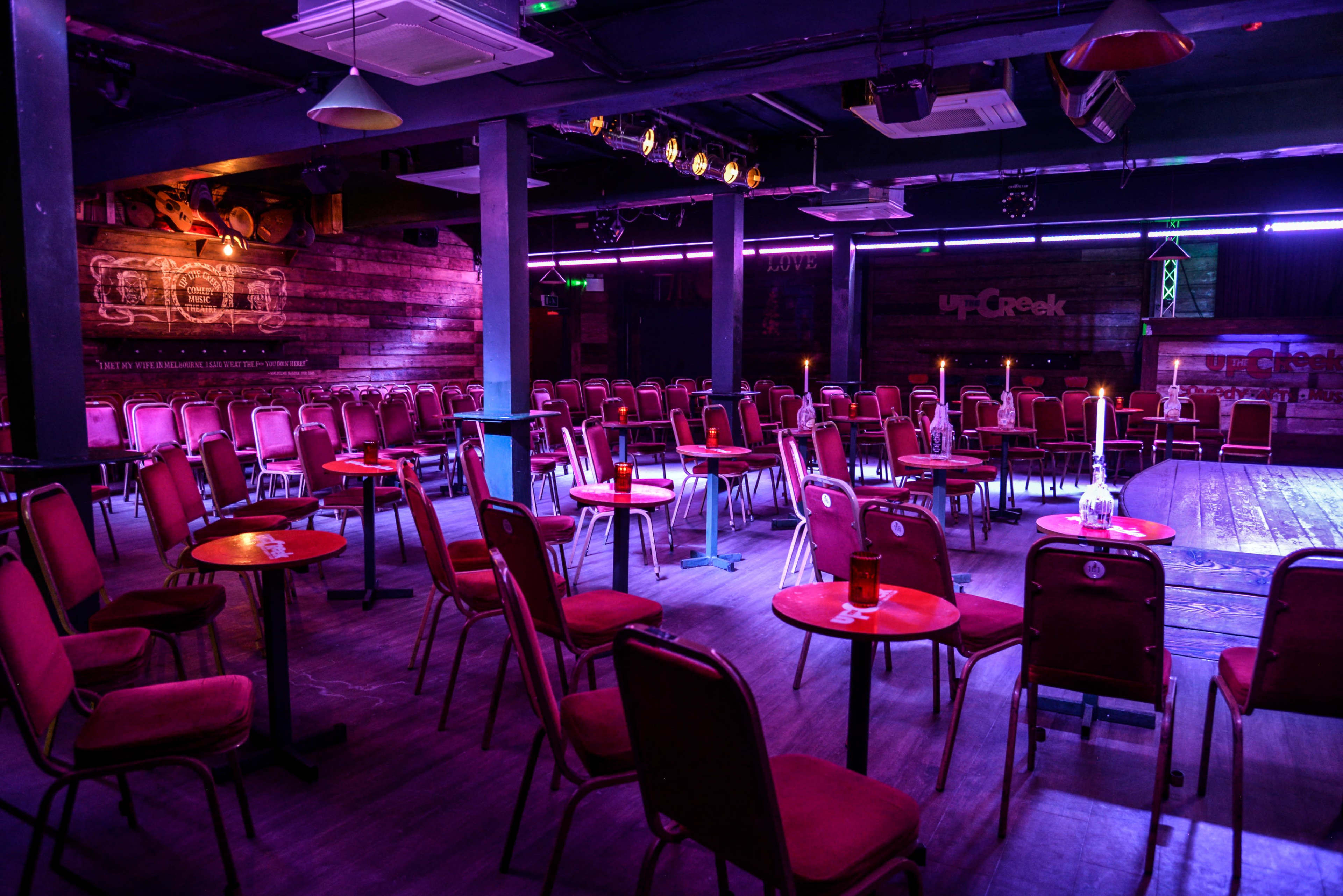 The image shows a dimly lit event space set up with rows of chairs and small tables, designed for an audience.