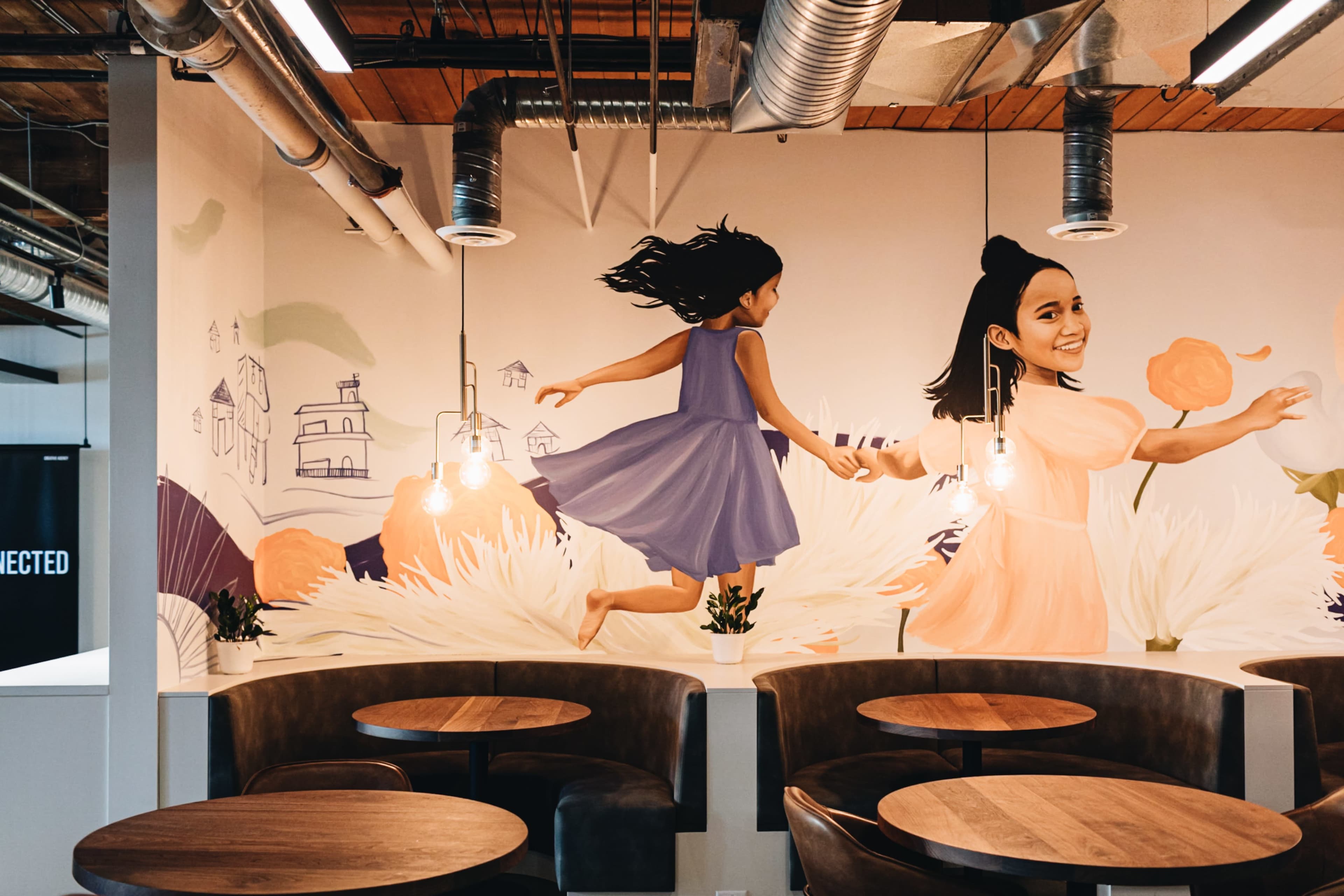 The image shows a mural featuring a young girl and a woman, along with several hanging light fixtures, above a dining area with wooden tables.