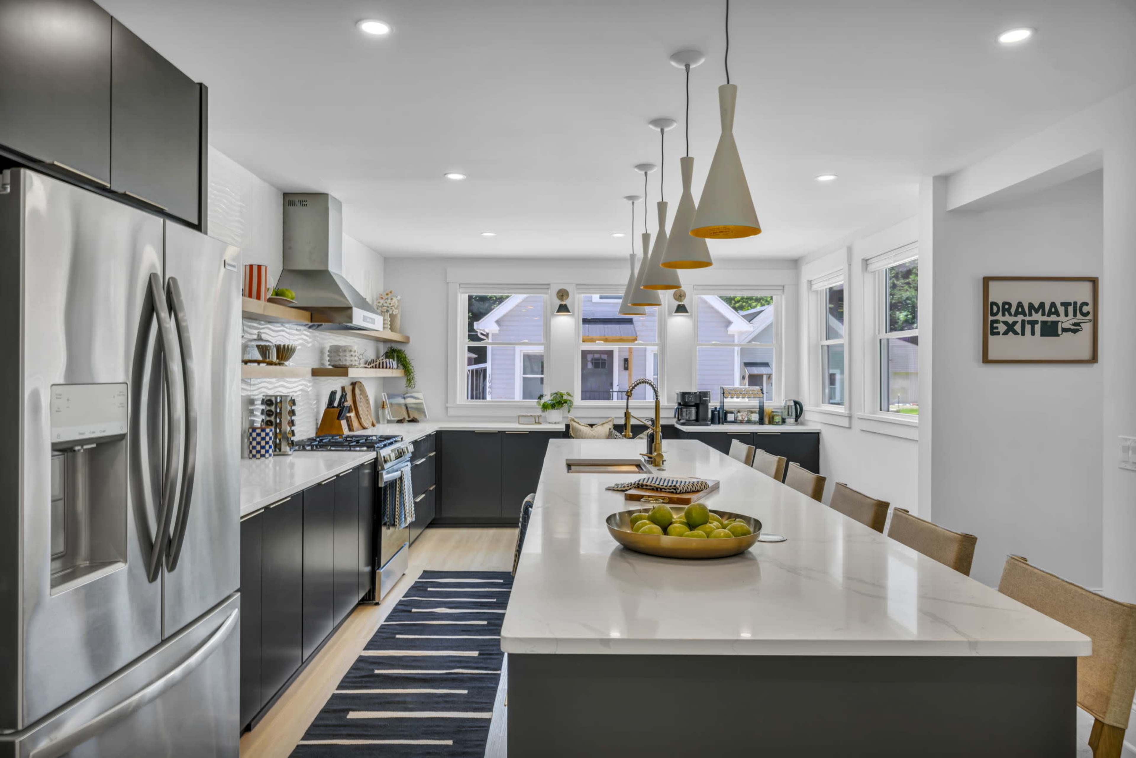 A modern kitchen features stainless steel appliances, a large island with seating, and white countertops under pendant lighting.