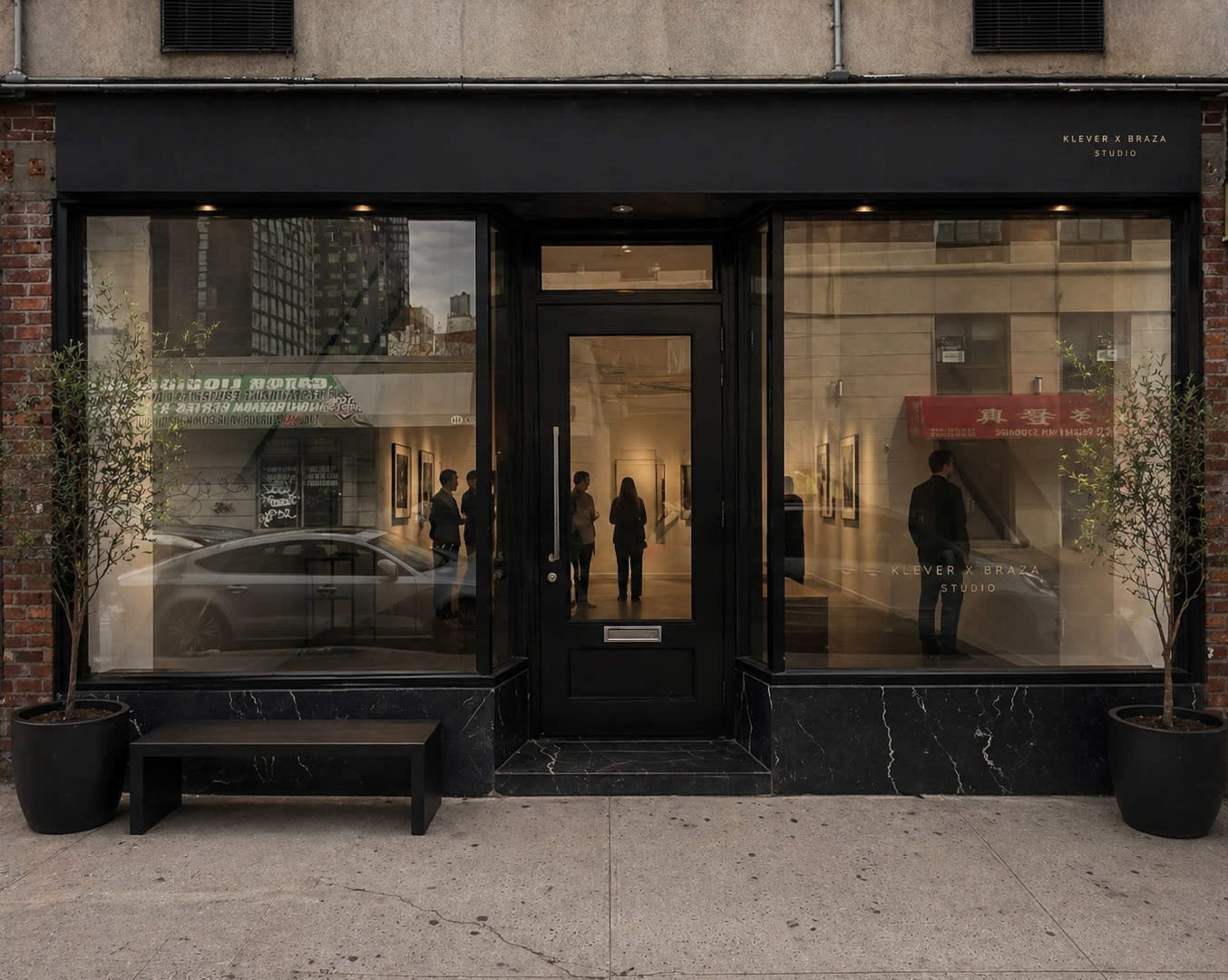 The image shows a modern art gallery with large glass windows, displaying a simple black door and a minimalist exterior design.