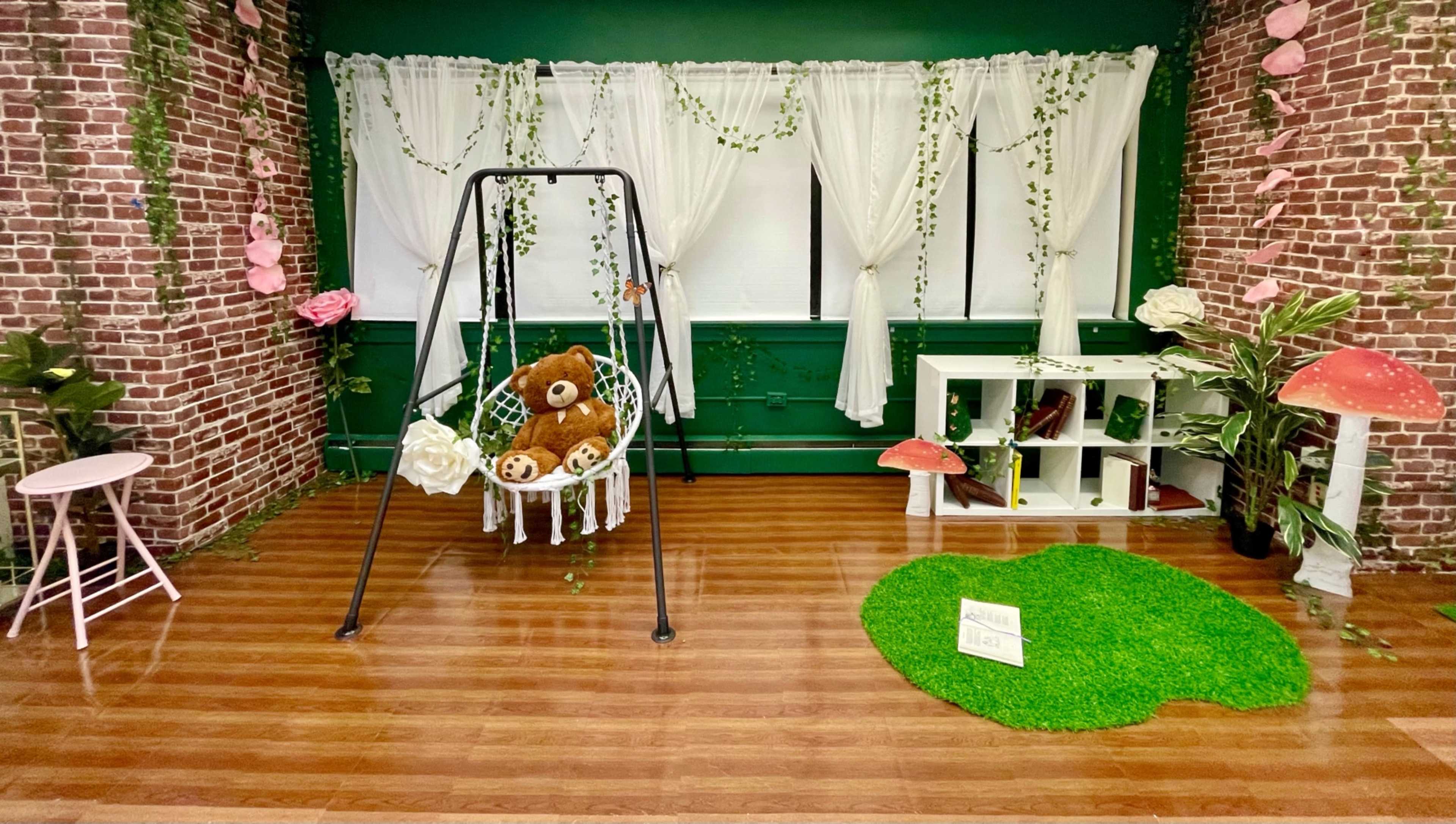 A cozy indoor setting with a swing, plush bears, a bookshelf, decorative mushrooms, and greenery against a brick wall.
