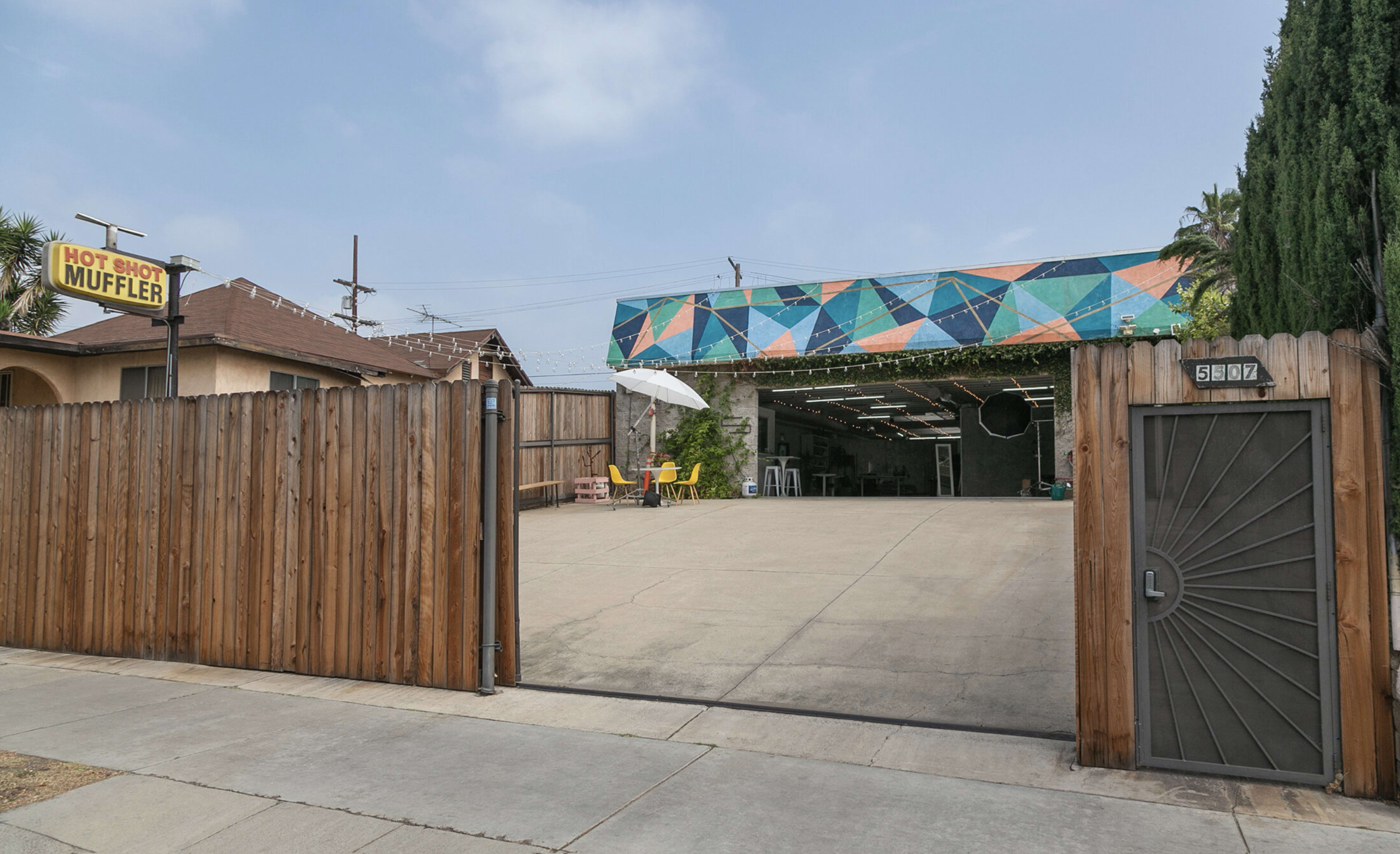 A fenced area with a concrete surface leads to a colorful building, marked by a sign for "Hot Shot Muffler" overhead.
