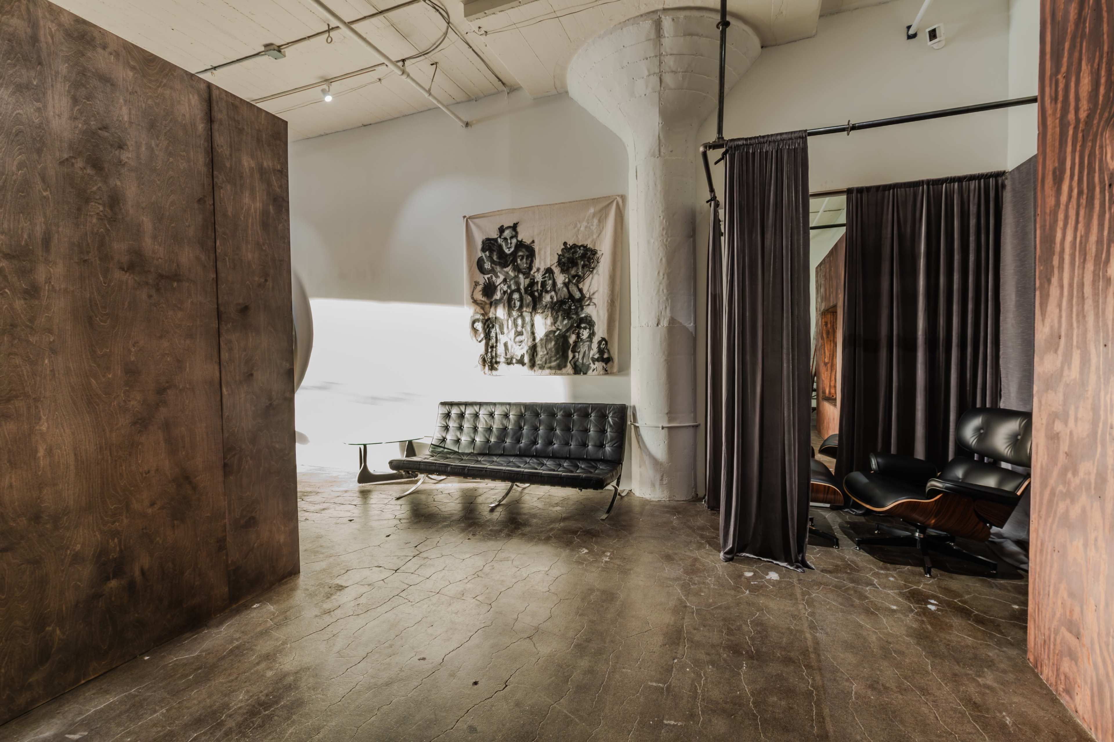 The image shows a spacious interior with a leather sofa, a large wall tapestry, and a seating area separated by curtains.