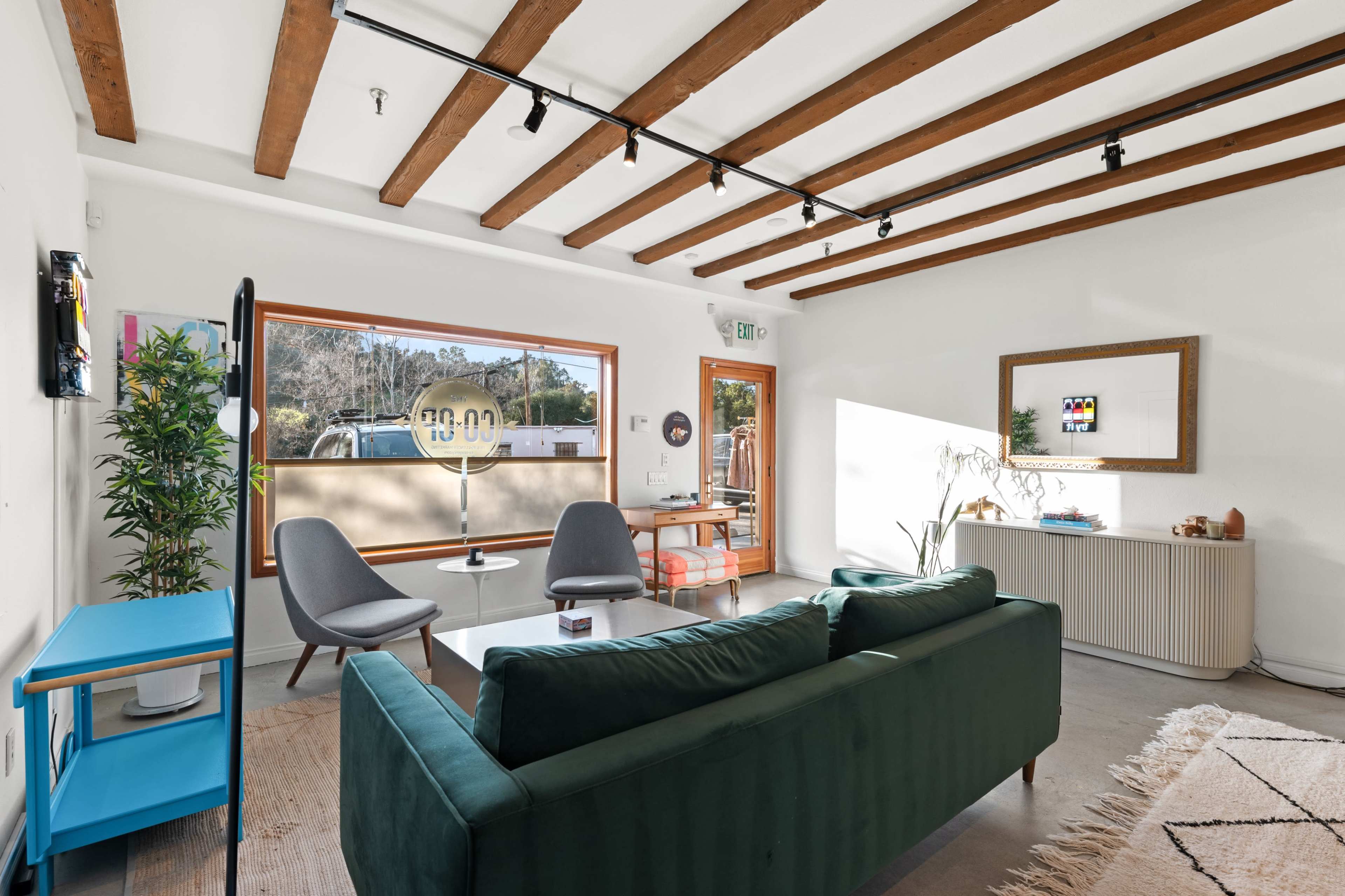 A modern living room features a green sofa, two gray chairs, a coffee table, and large windows that provide natural light.