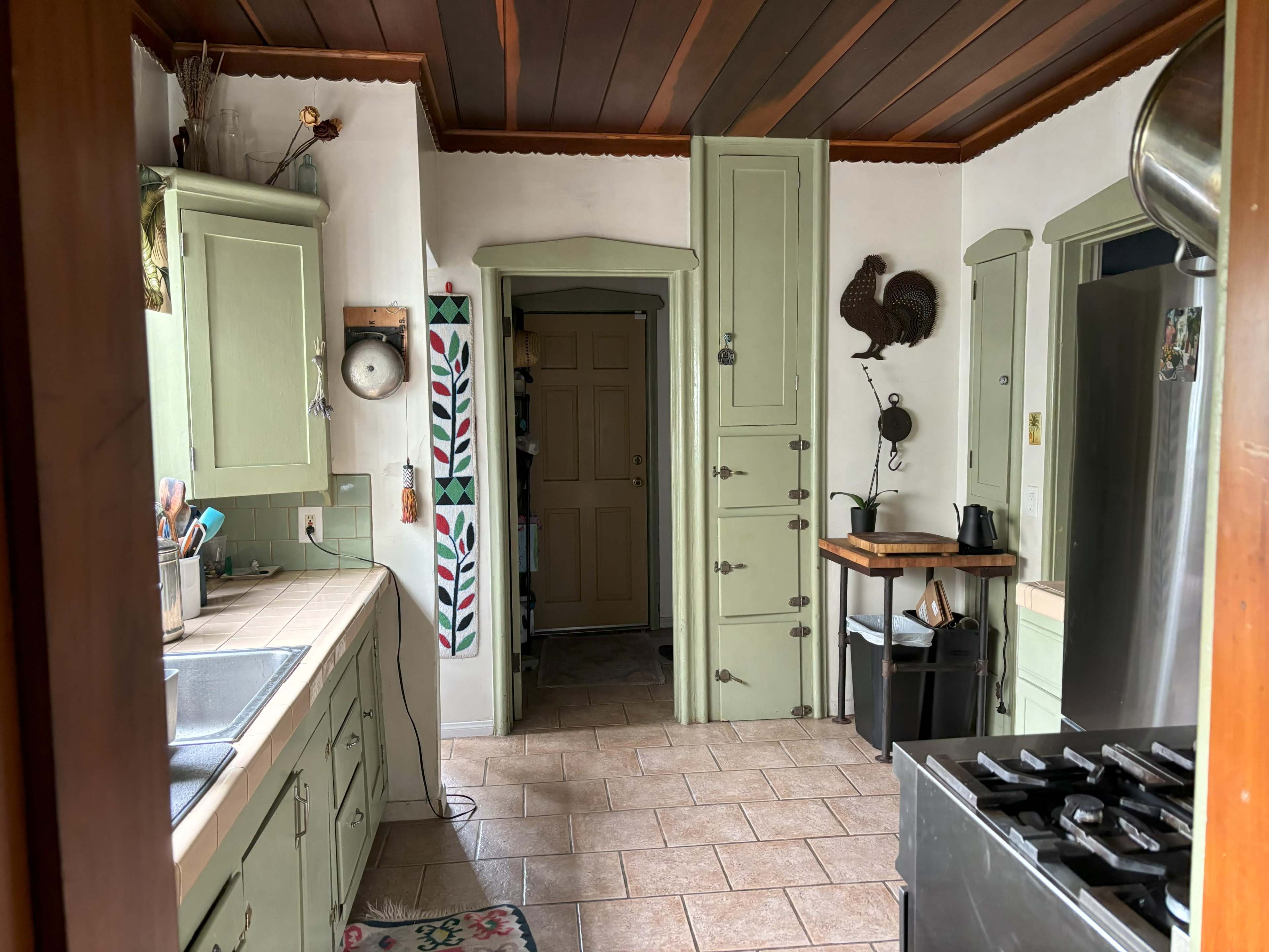 A kitchen with green cabinets, a stainless steel refrigerator, and a doorway leading to another room.