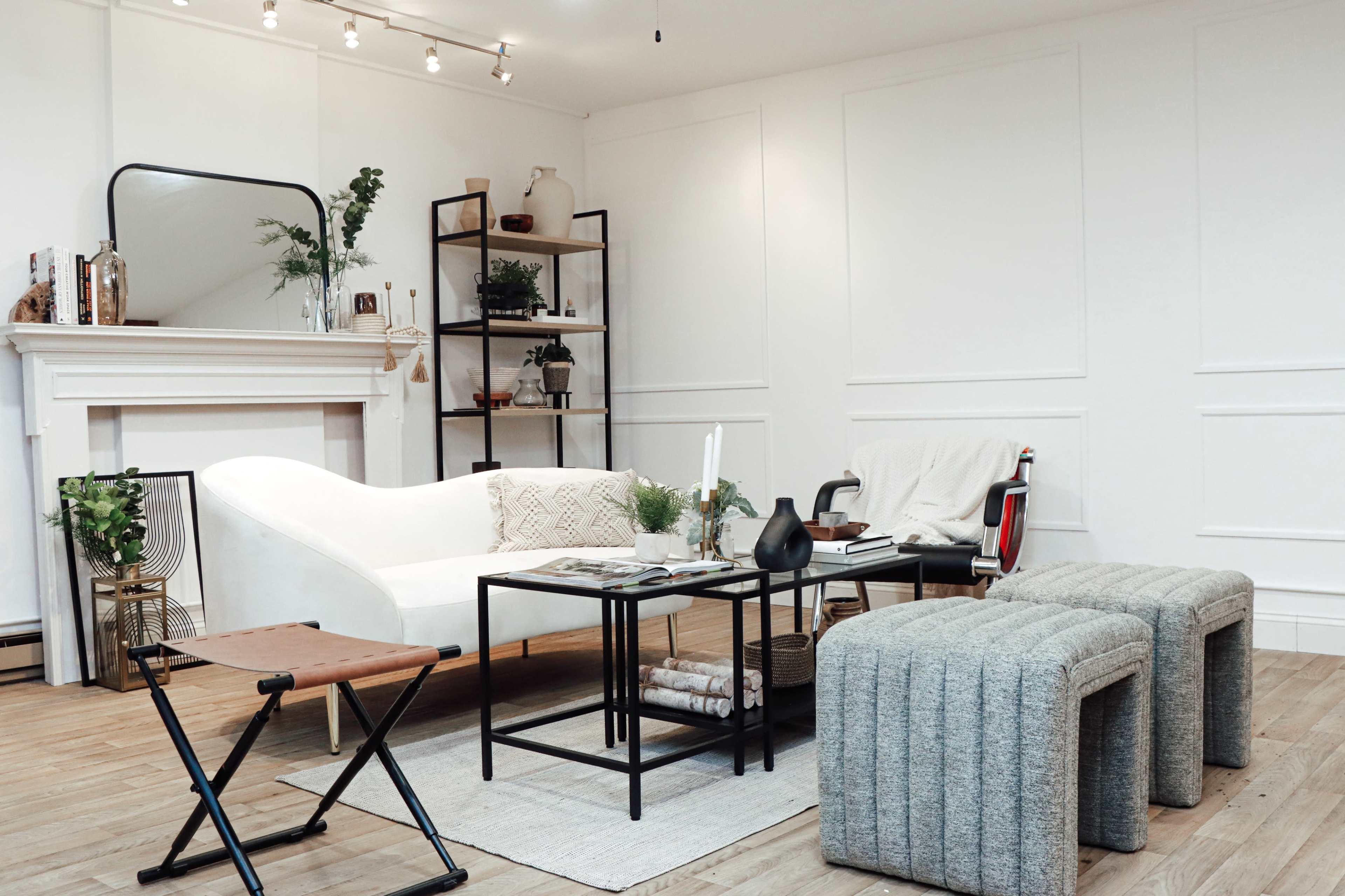 A modern living room with a white couch, a coffee table, two textured stools, and a bookshelf against a light-colored wall.