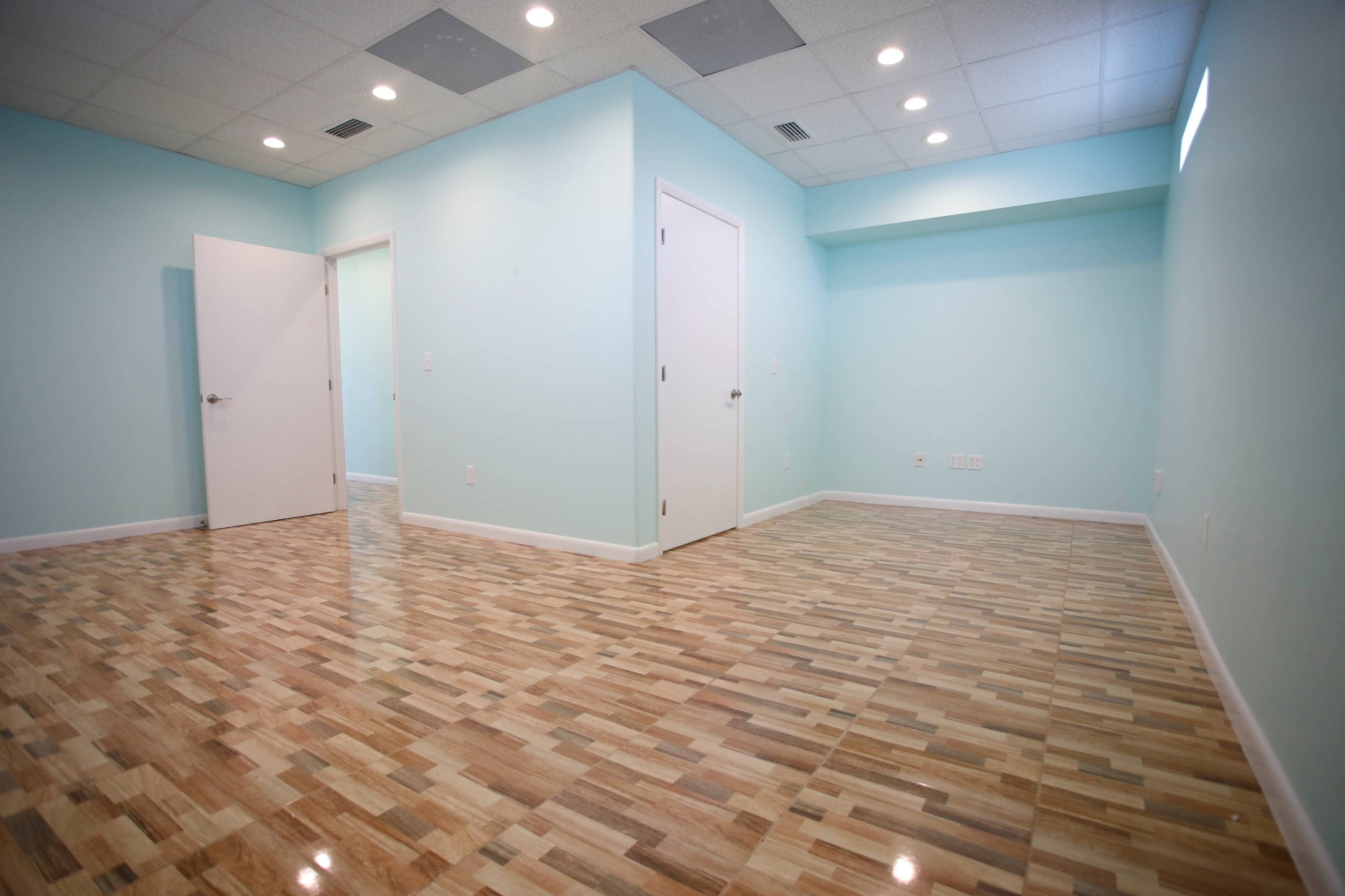 The image shows an empty room with light blue walls, a wooden floor, and two white doors.