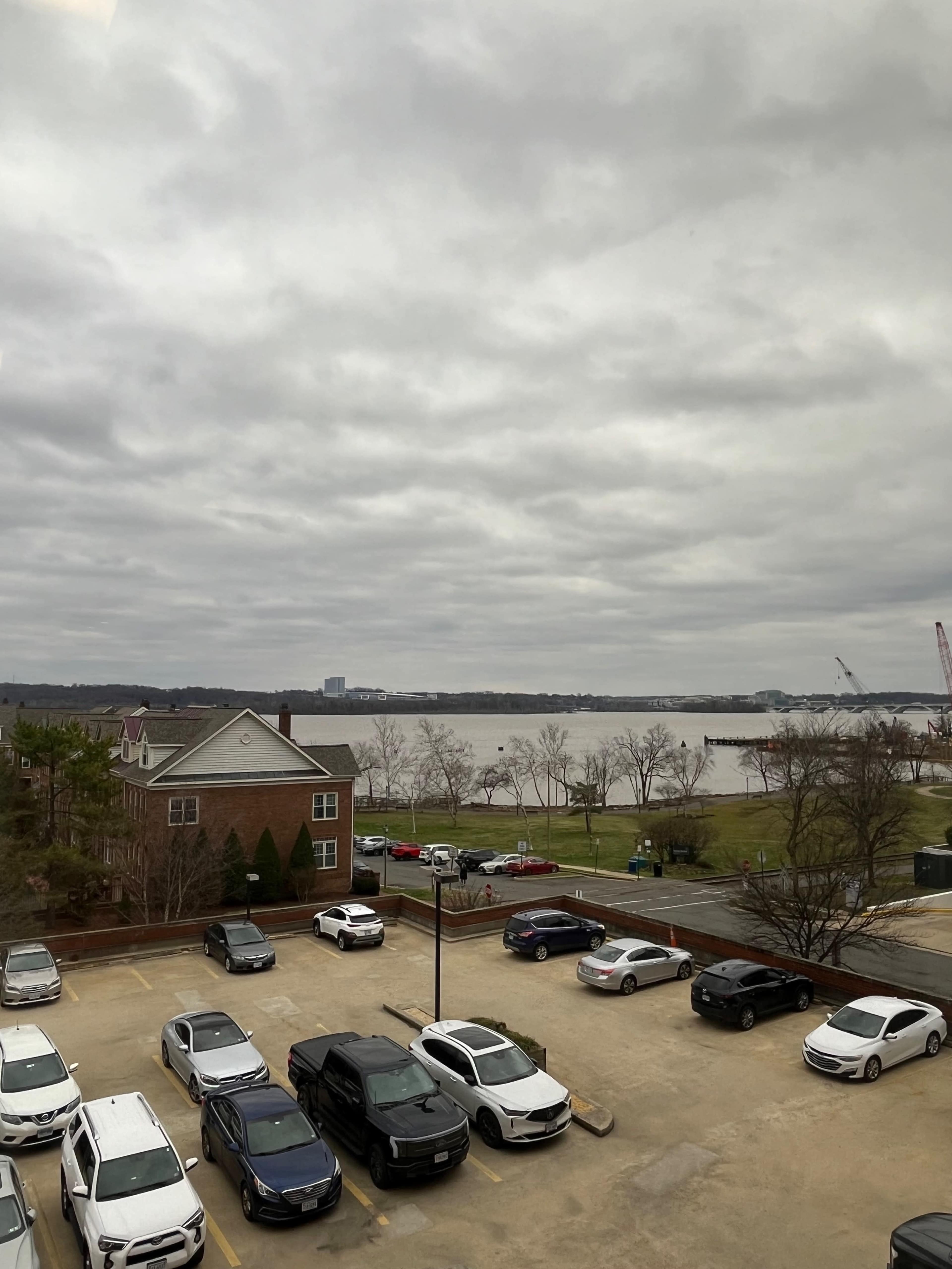 A parking lot with several cars parked, overlooking a river and a cloudy sky in the background.