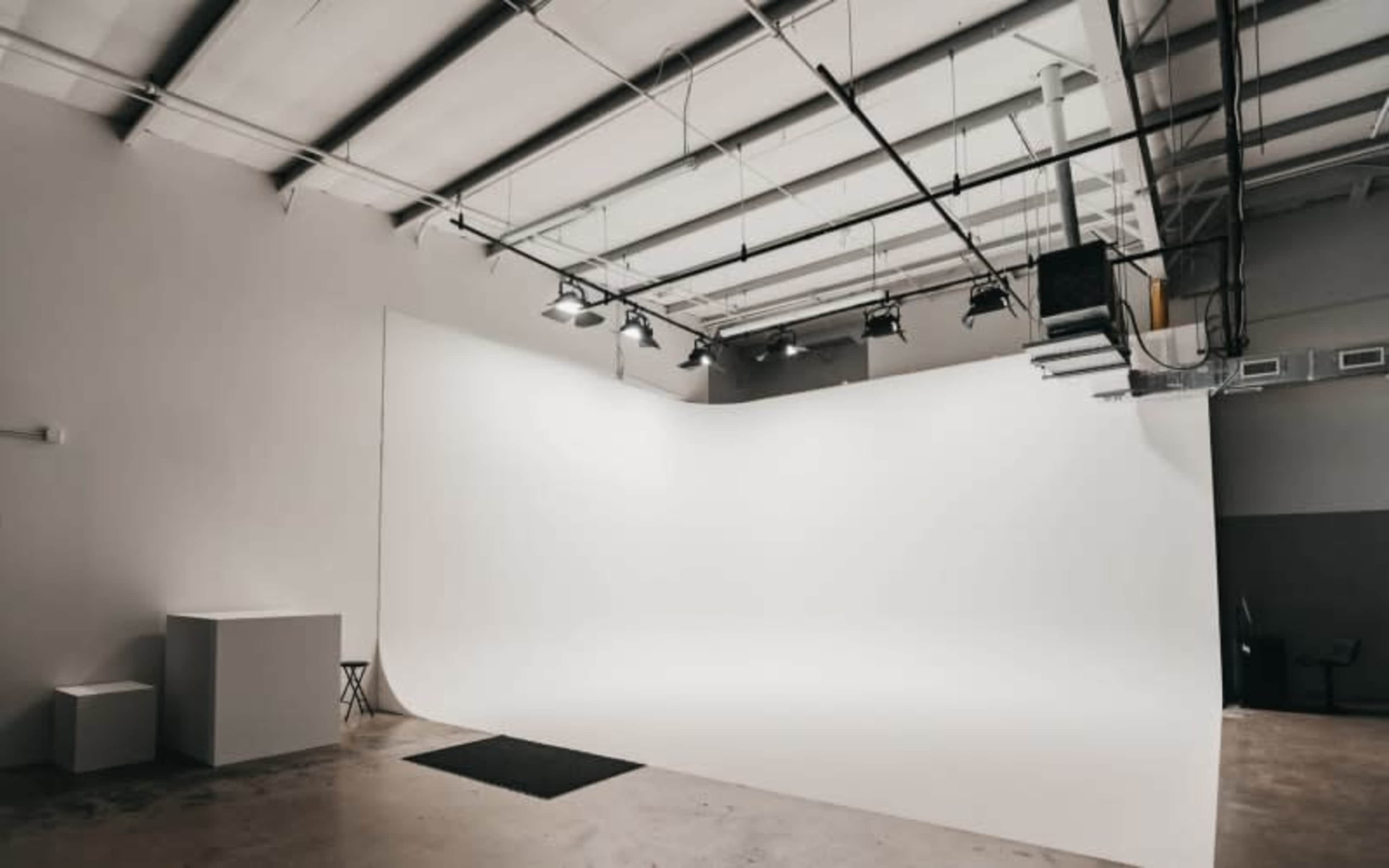 The image shows a spacious, empty photo studio with a large curved white backdrop and overhead lighting.