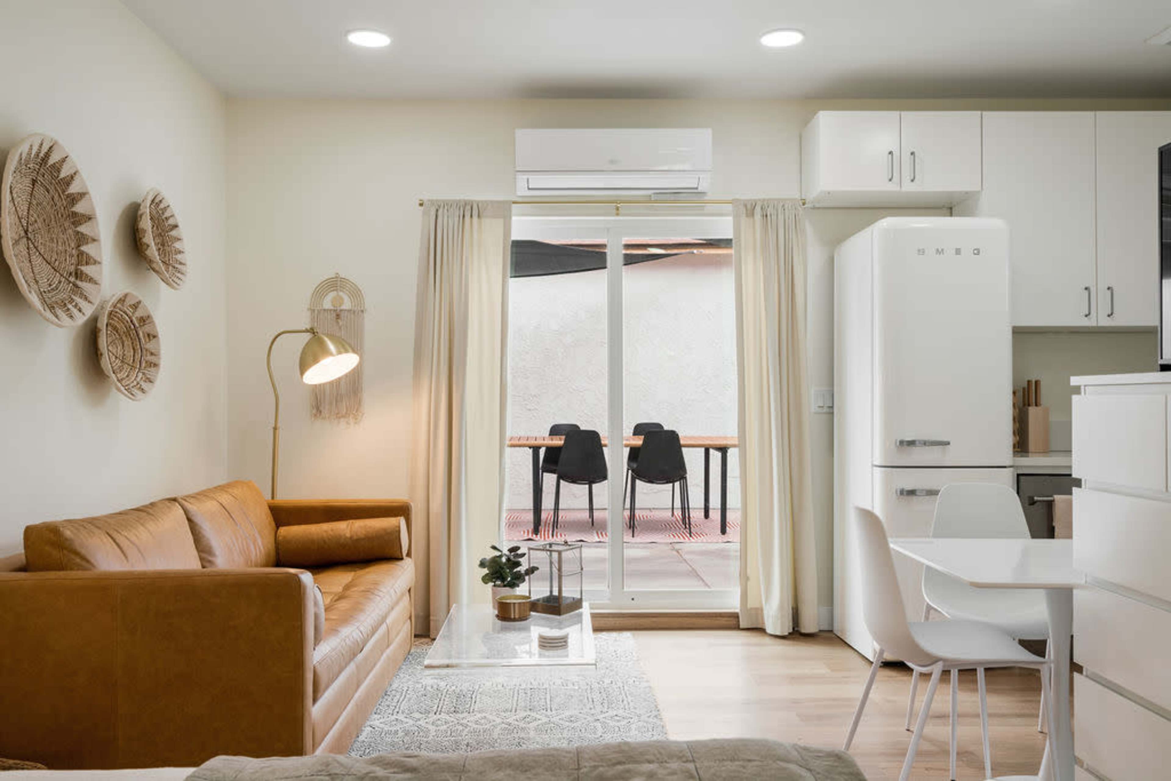 A cozy living space featuring a brown leather sofa, a white dining table, and sliding glass doors leading to an outdoor area with chairs.