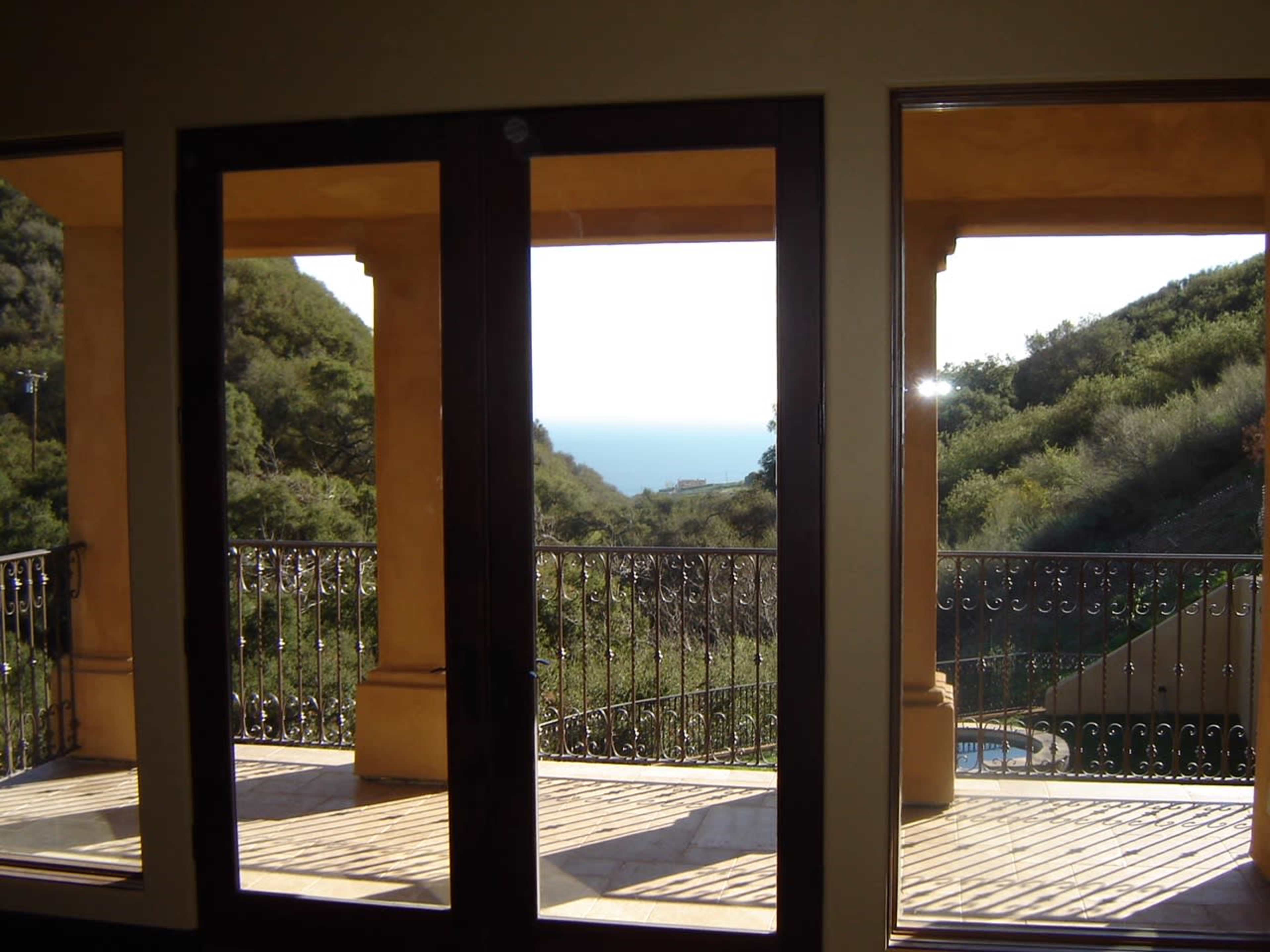 The image shows a view from a large window overlooking a wooden deck and a distant ocean view framed by hills.