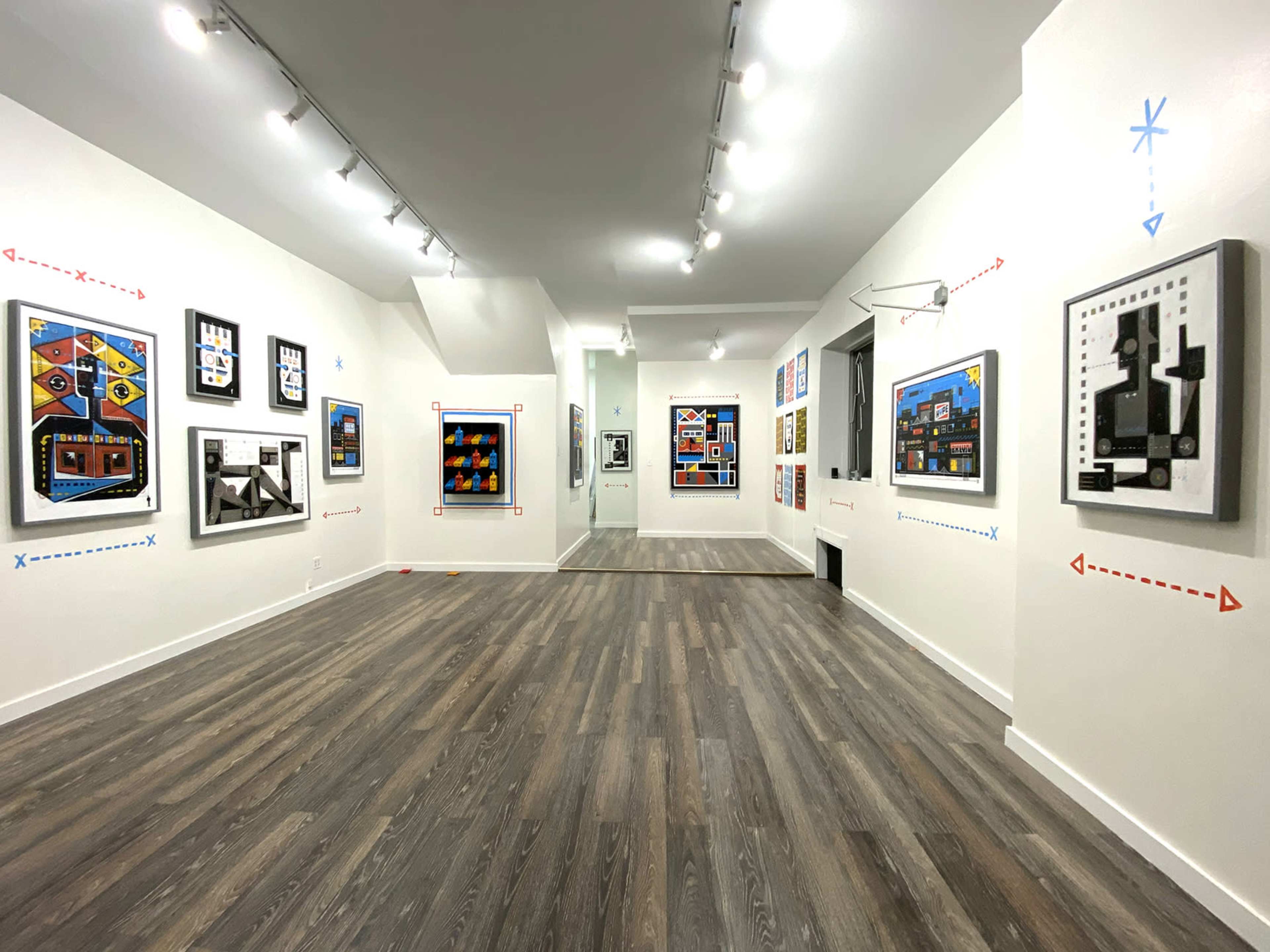 An art gallery with several colorful framed artworks displayed on white walls and a wooden floor.
