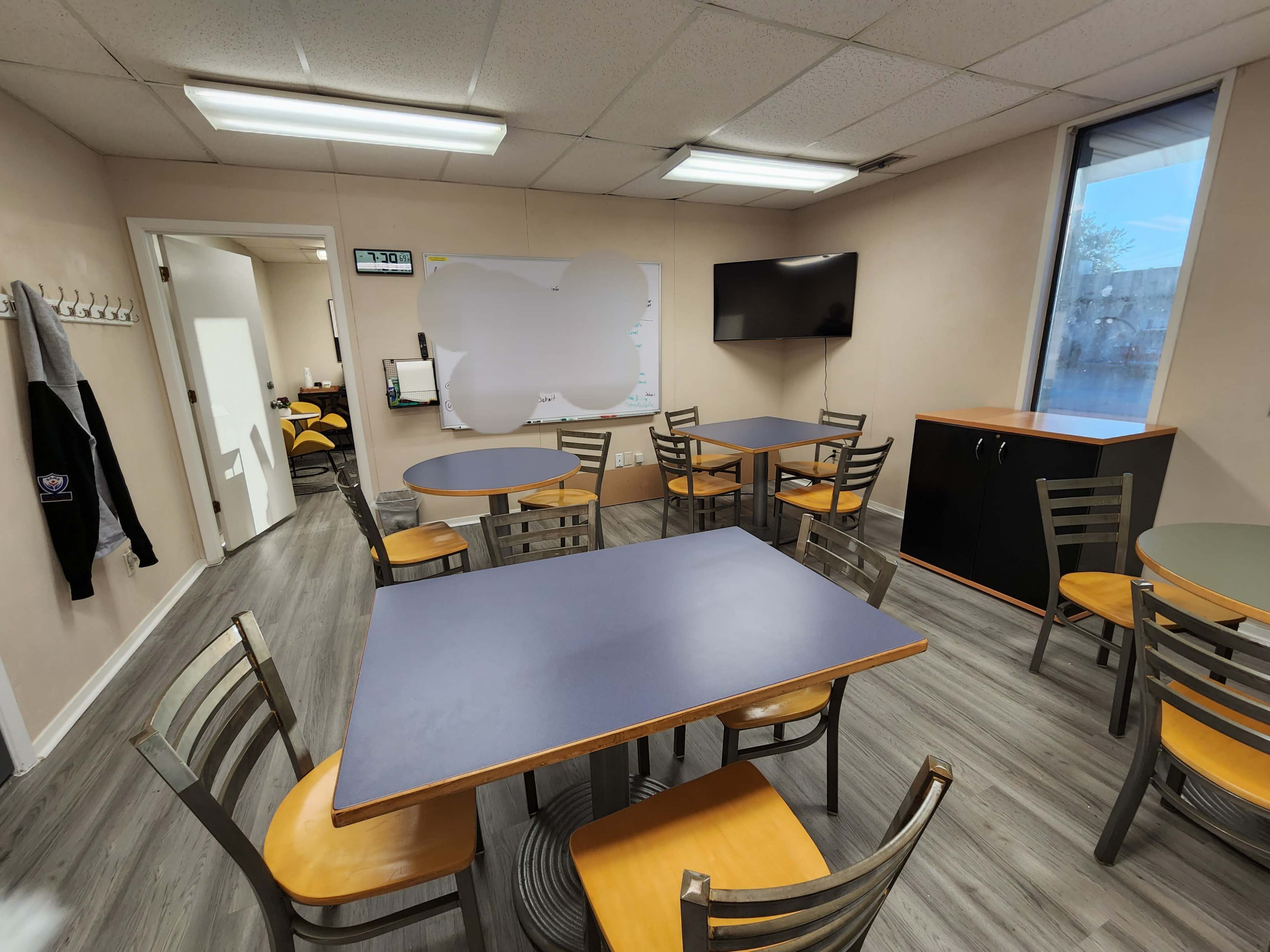 A well-lit break room featuring multiple tables and chairs, a wall-mounted television, and a whiteboard.