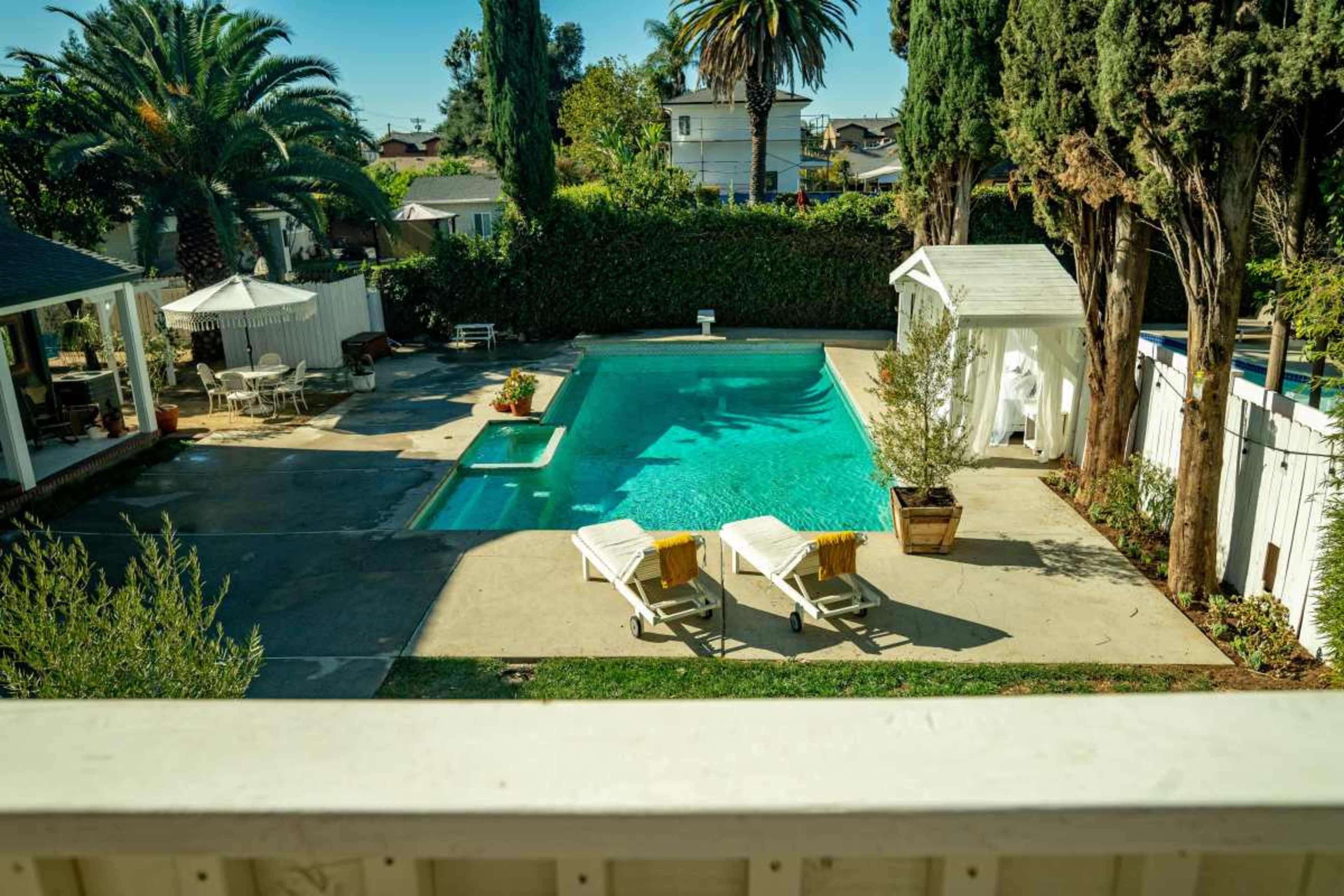 The image shows a well-maintained backyard with a swimming pool, two lounge chairs, palm trees, and a white gazebo.