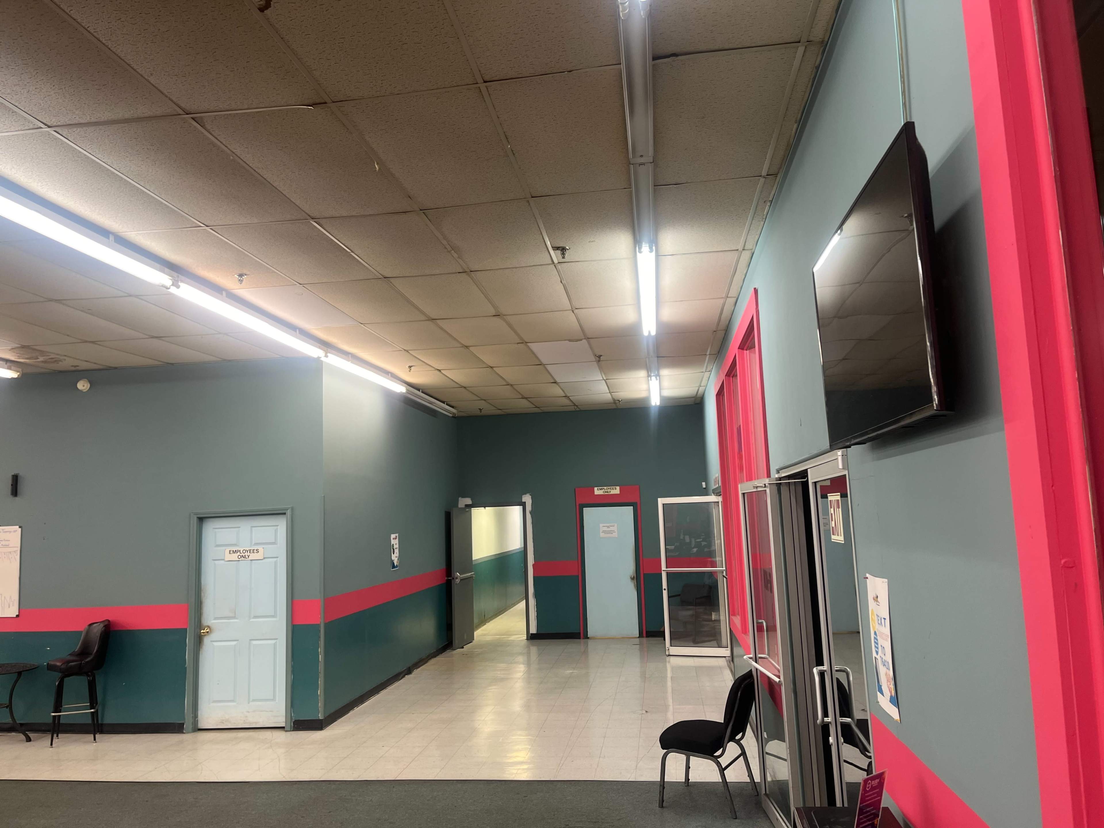 An empty hallway with teal walls, pink accents, and a wall-mounted television.