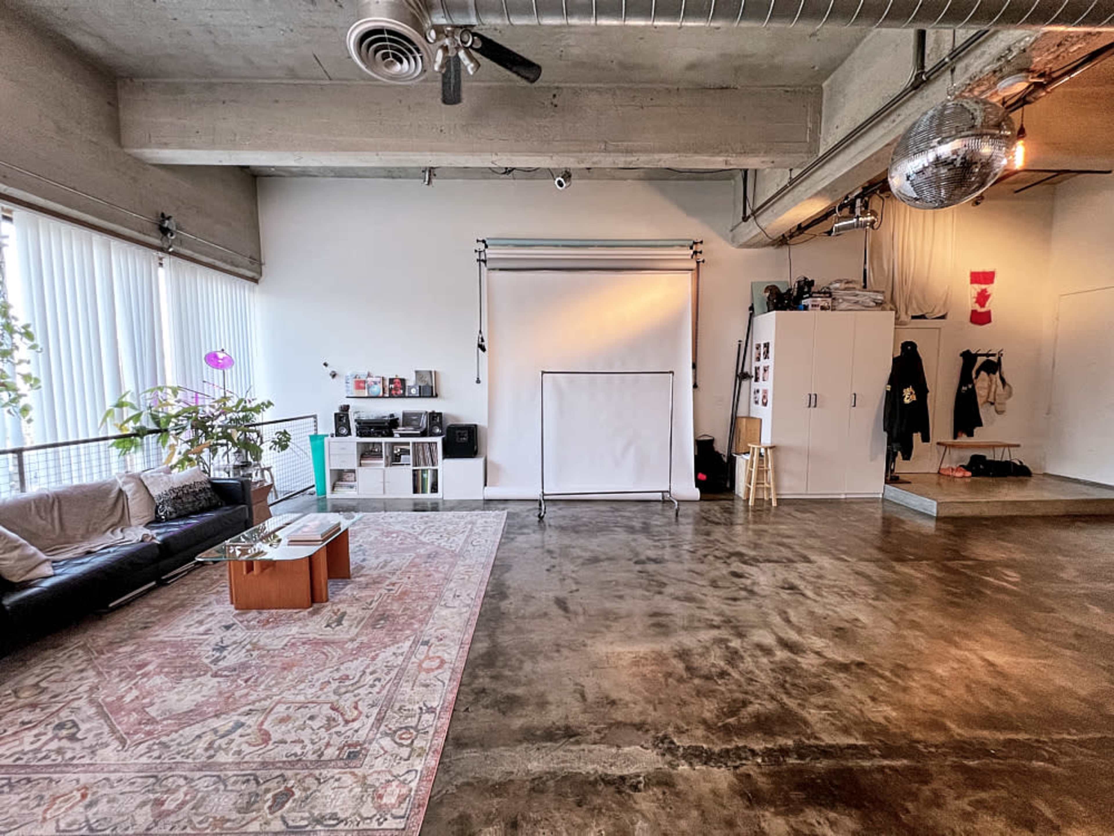 A spacious, industrial-style room with polished concrete floors, a seating area with a couch, a backdrop setup for photography, and storage cabinets along the wall.