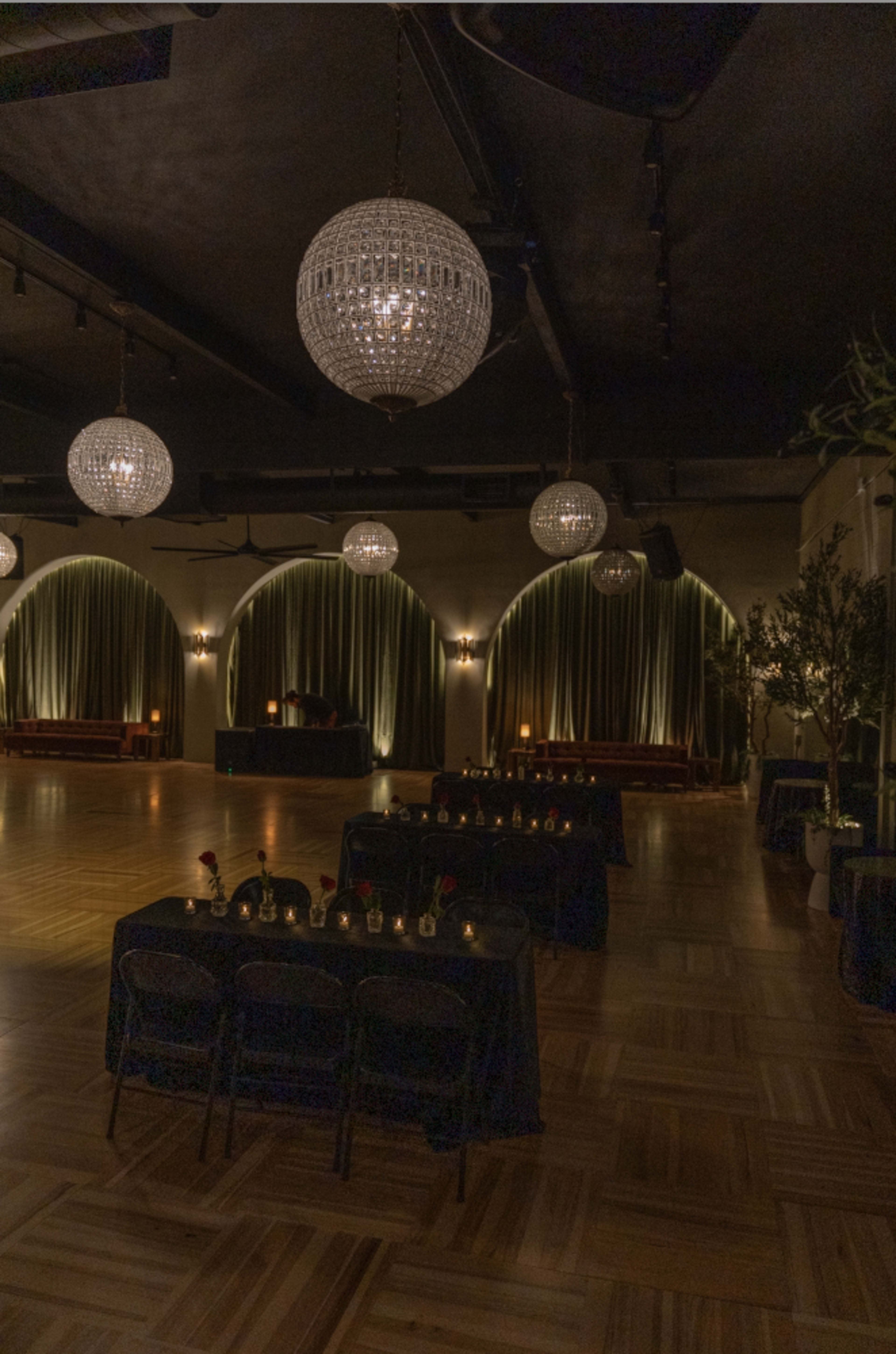 A spacious event venue features tables with candles, dark chairs, and large crystal chandeliers hanging from the ceiling.