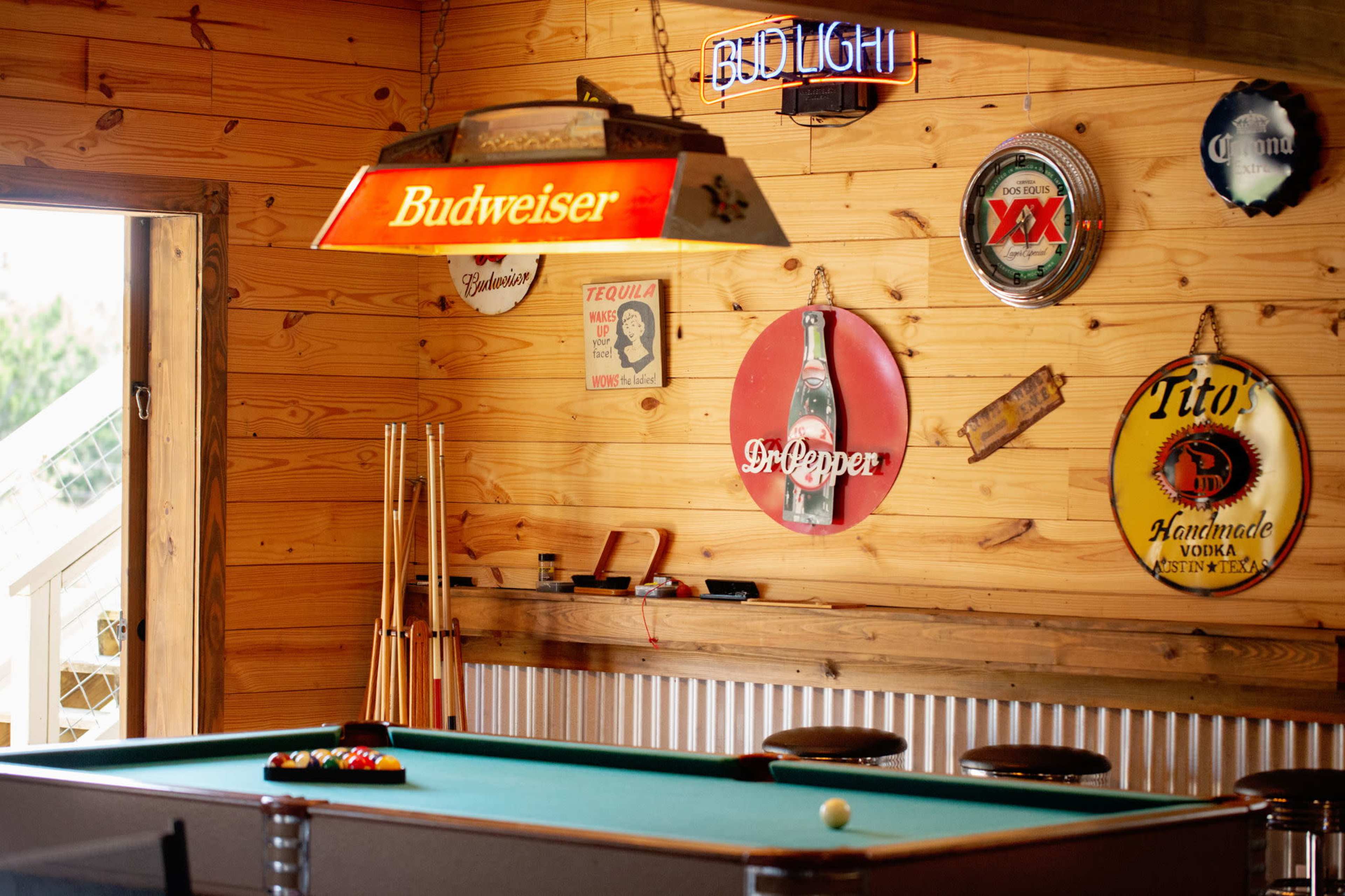 The image shows a wooden-paneled room with a pool table, a Budweiser lamp hanging over it, and various beer advertisements on the walls.