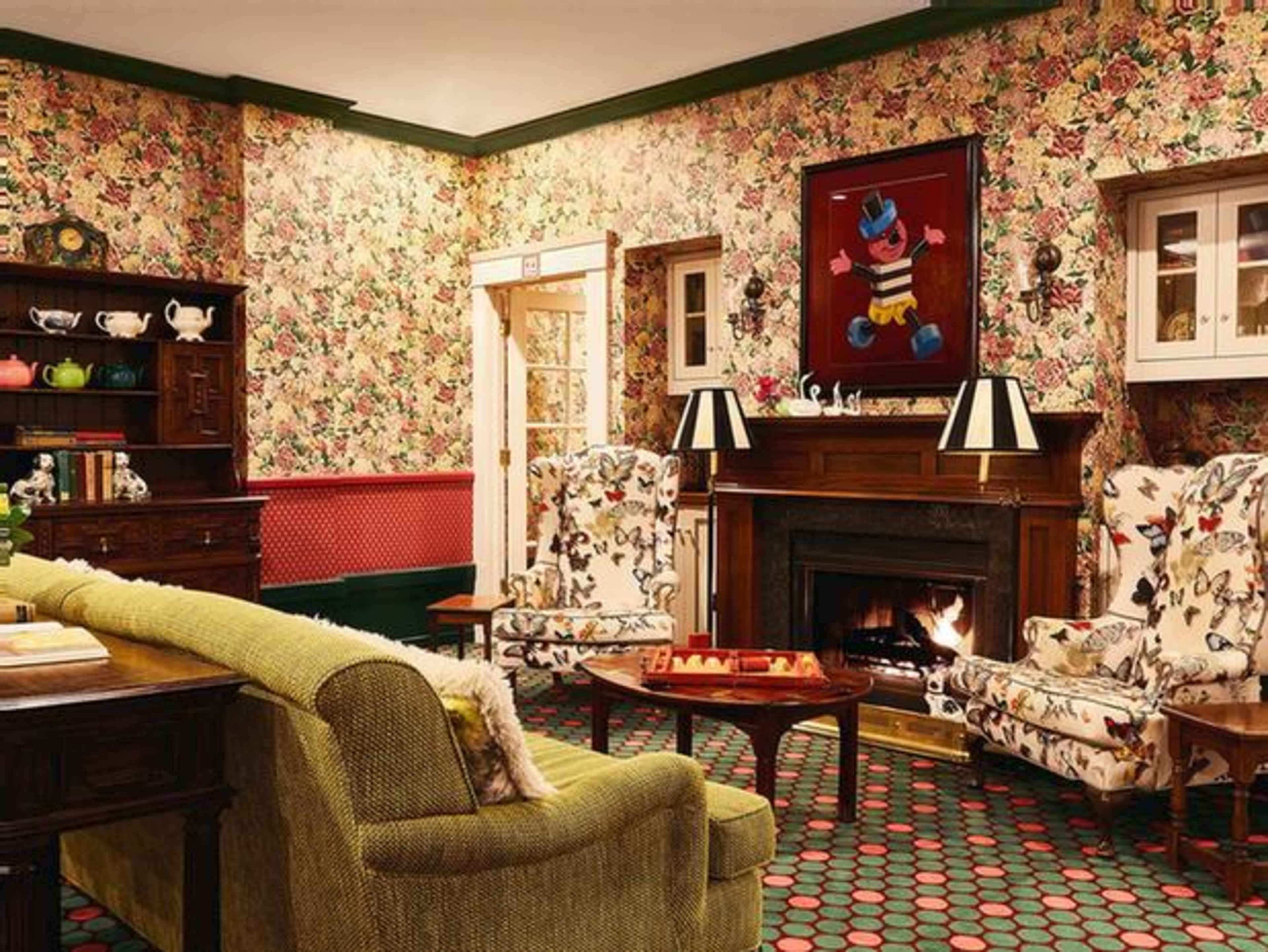 The living room features floral wallpaper, a fireplace, patterned armchairs, and a green sofa, creating a cozy atmosphere.