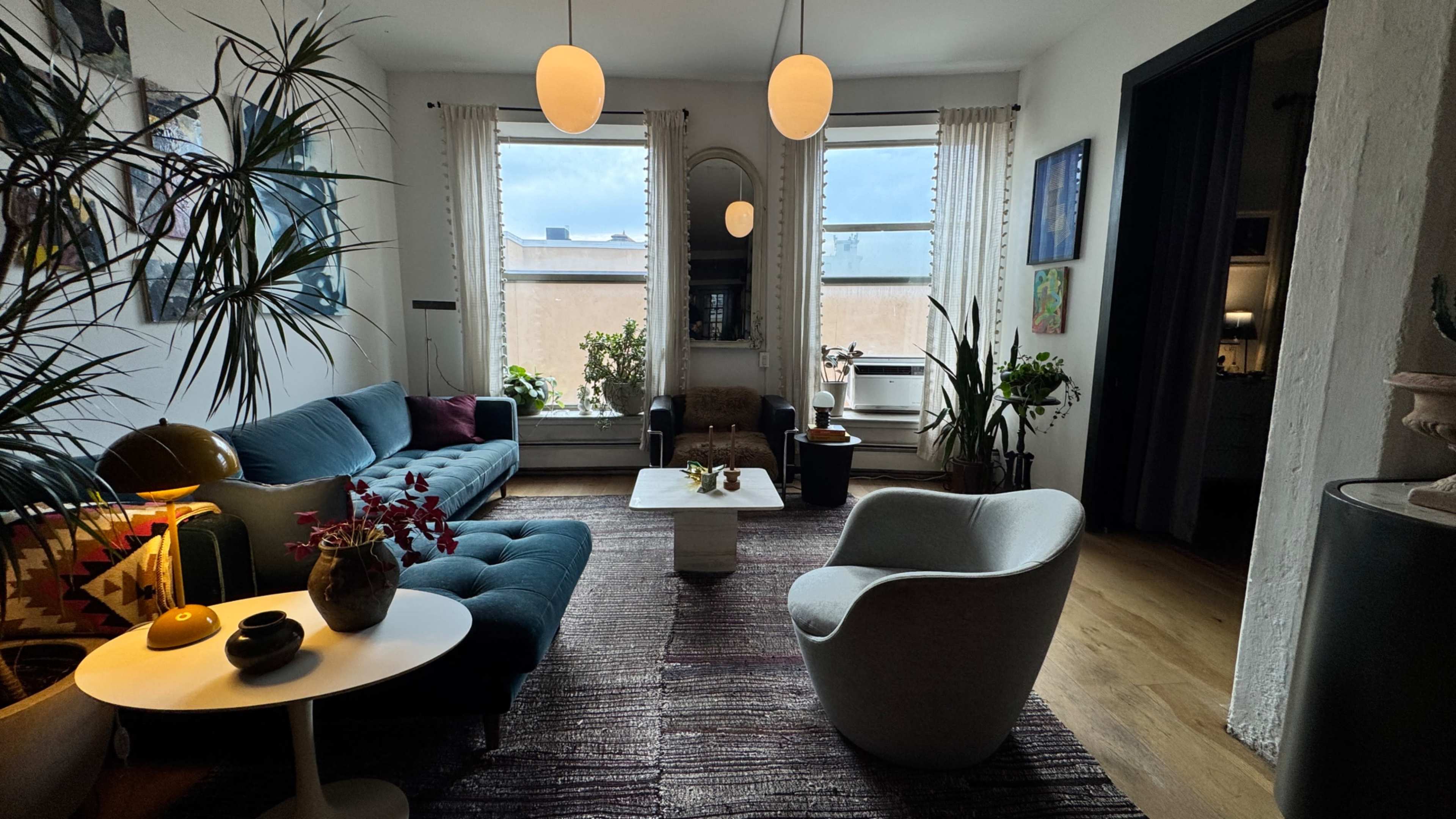 The room features a cozy living space with a blue sofa, a light-colored coffee table, and large windows allowing natural light to fill the area.