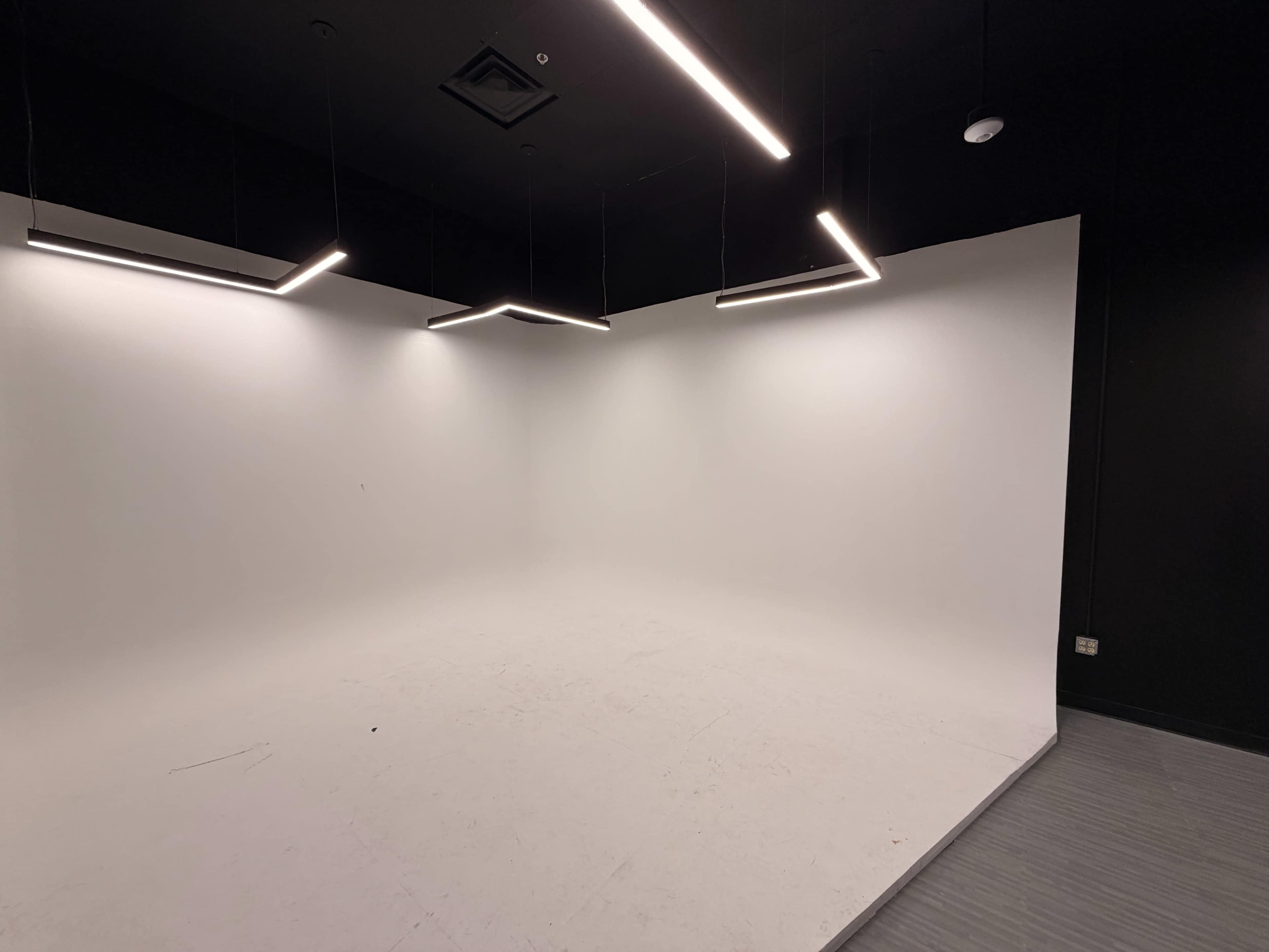 The image shows a minimalist studio space with a plain white wall and modern linear overhead lights.