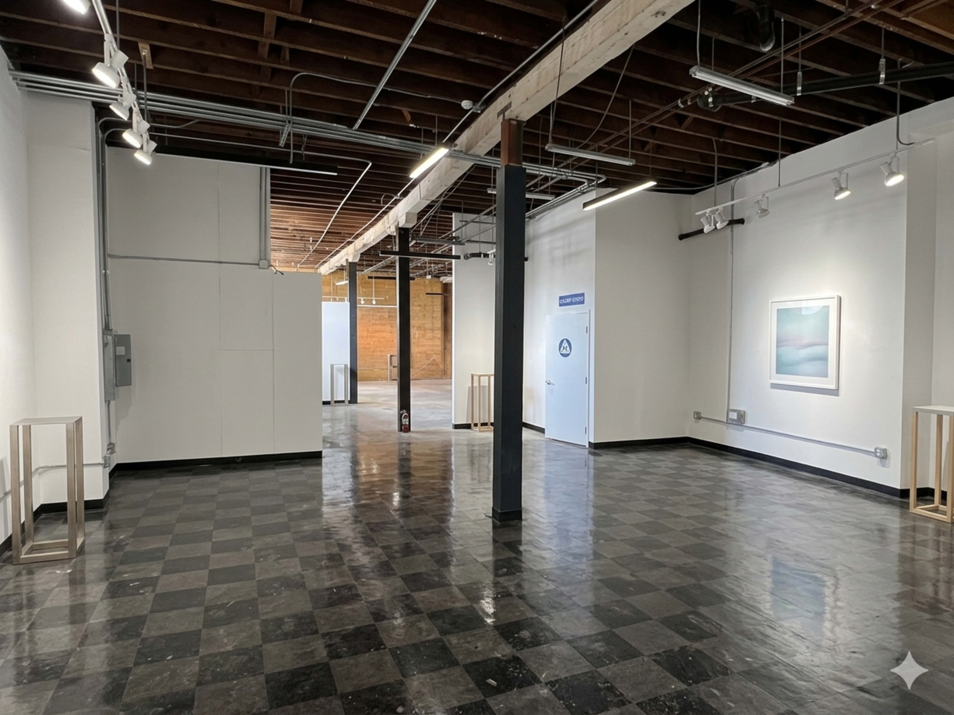 The image shows a spacious, modern art gallery with polished black and white checkered flooring, white walls, and exposed wooden beams in the ceiling.