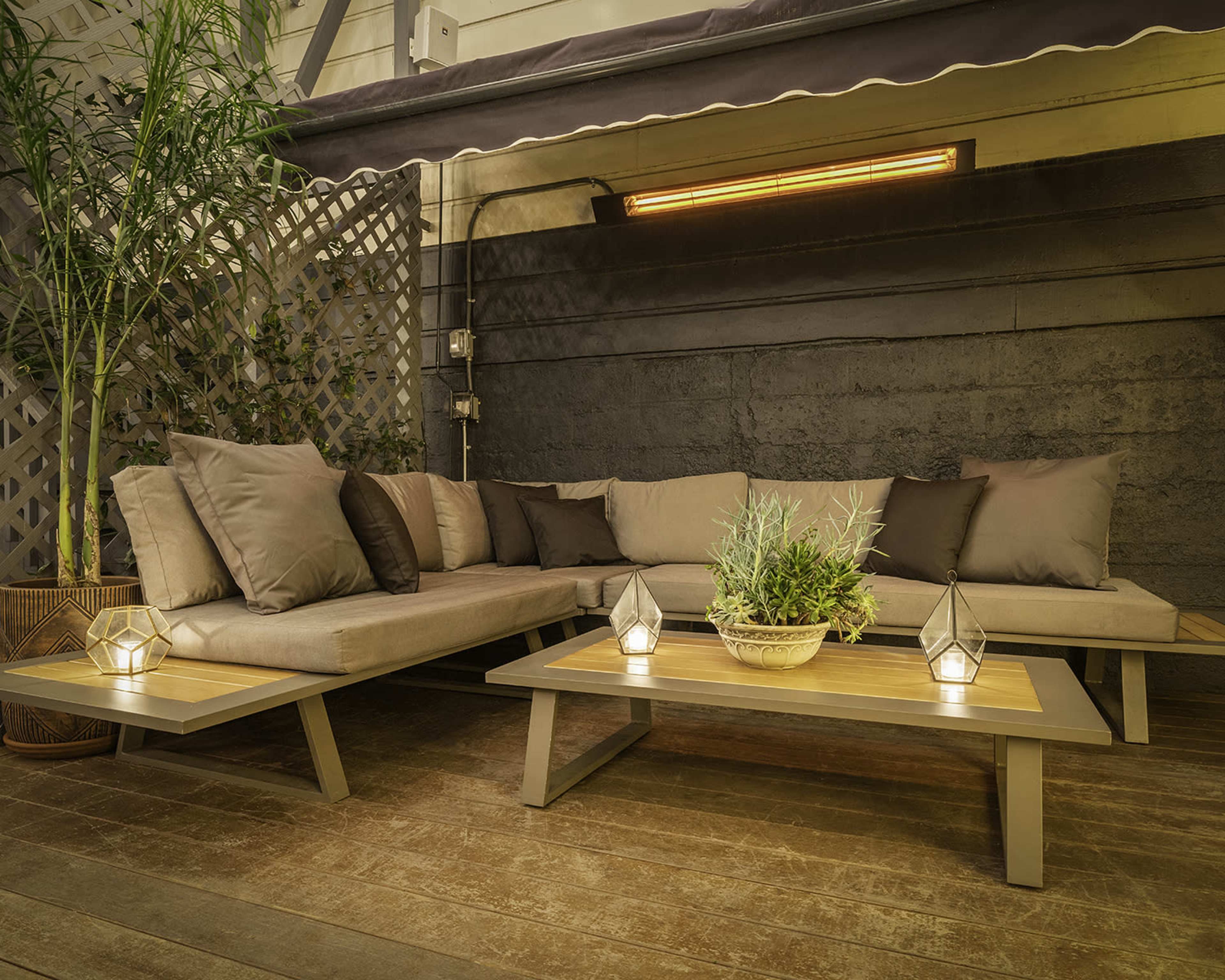 A modern outdoor seating area features a sectional sofa with brown cushions, a wooden coffee table, and decorative lanterns on a wooden deck.