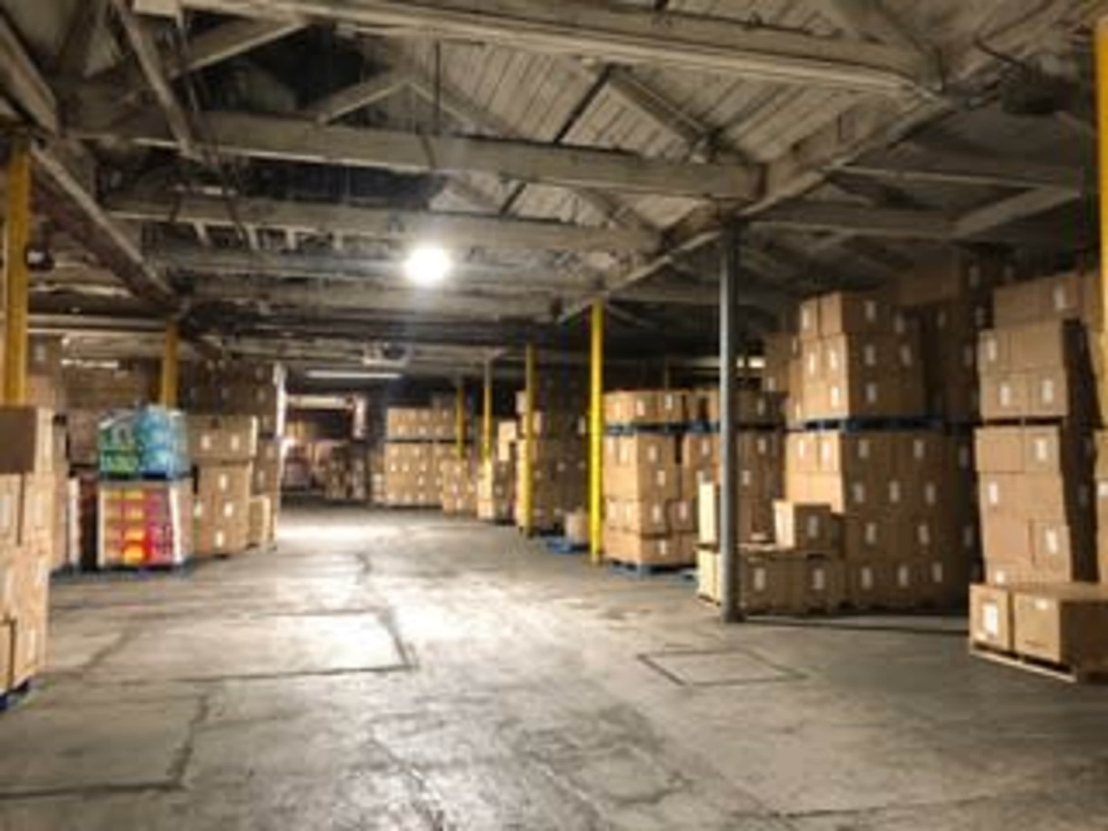 The image shows a large warehouse filled with stacked cardboard boxes organized along the walls and aisles.
