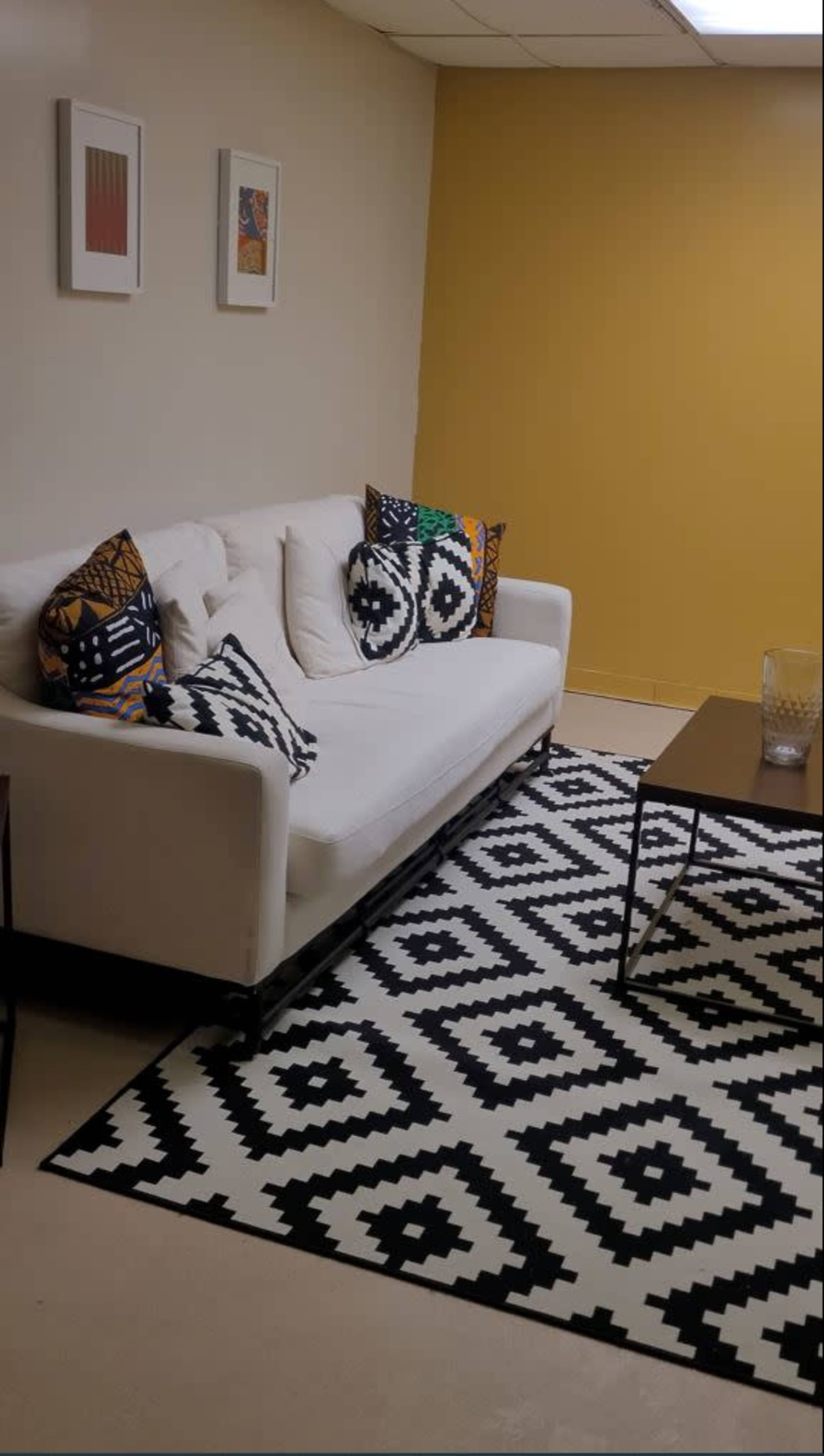 The image shows a cozy living room with a white sofa adorned with patterned pillows, a geometric black and white rug on the floor, and a dark coffee table nearby.