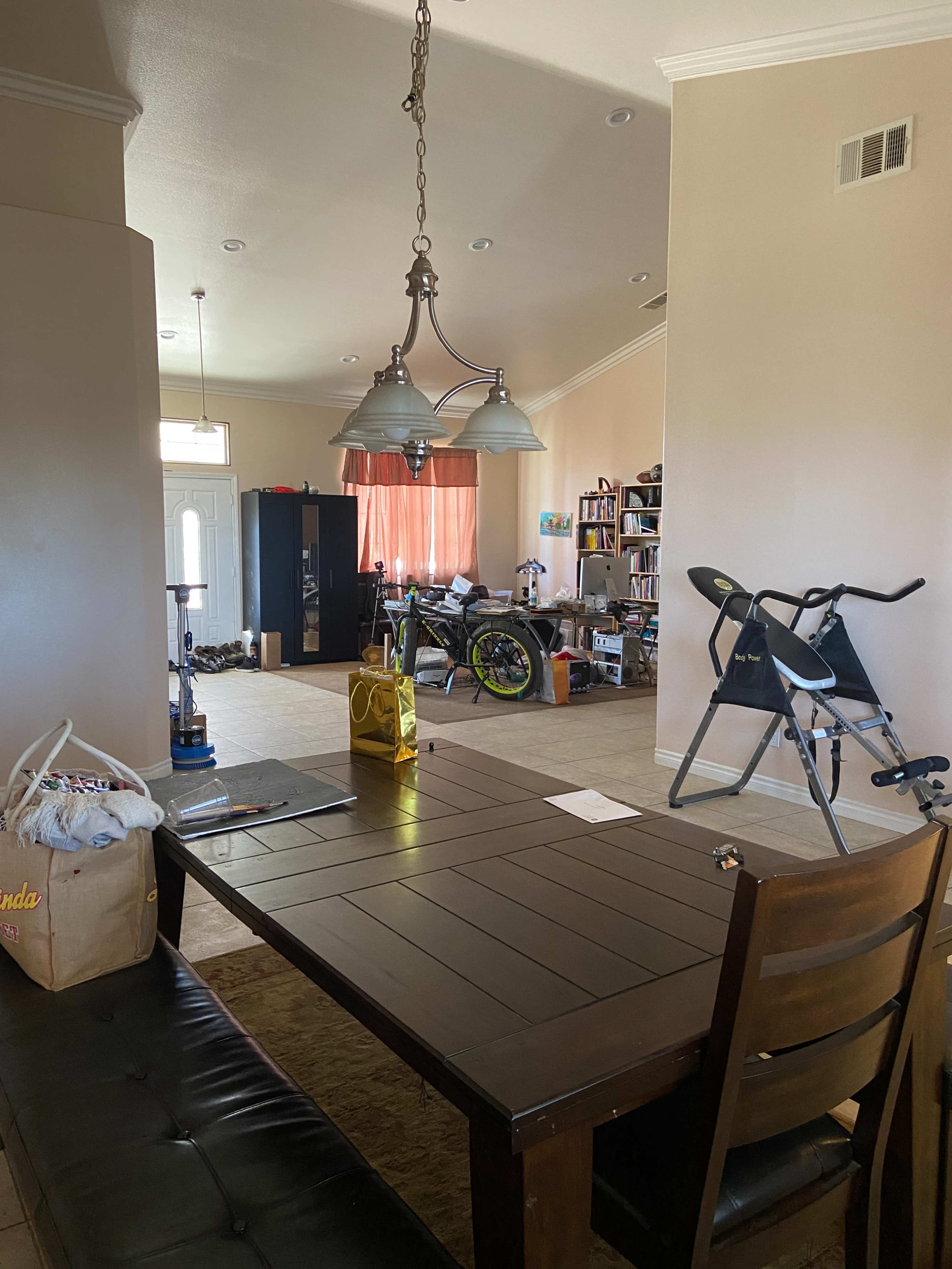 A dining table is positioned in the foreground of a cluttered living space that features a bicycle, stroller, and various items scattered around.