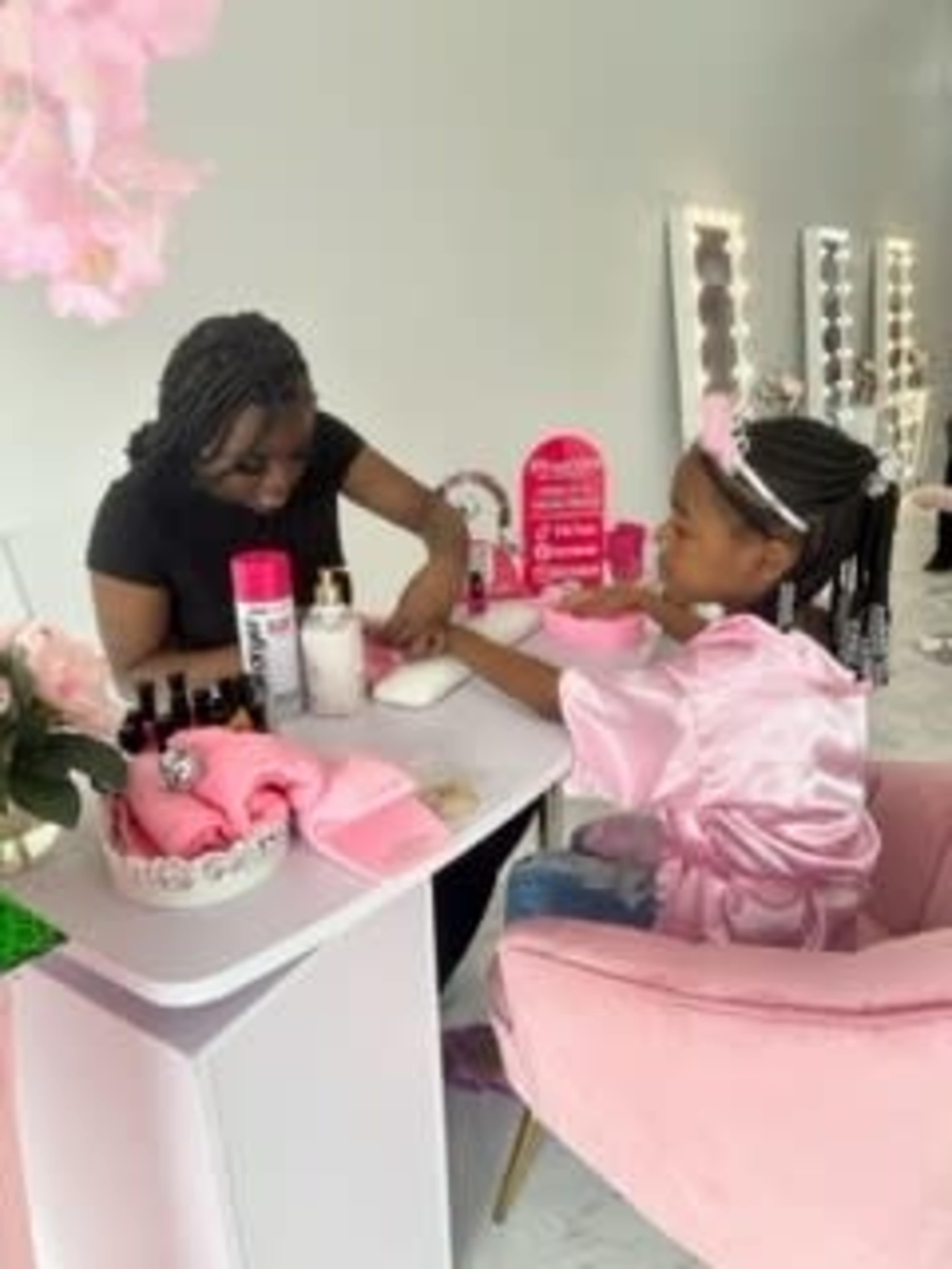 A woman helps a girl with a manicure at a well-decorated beauty station.