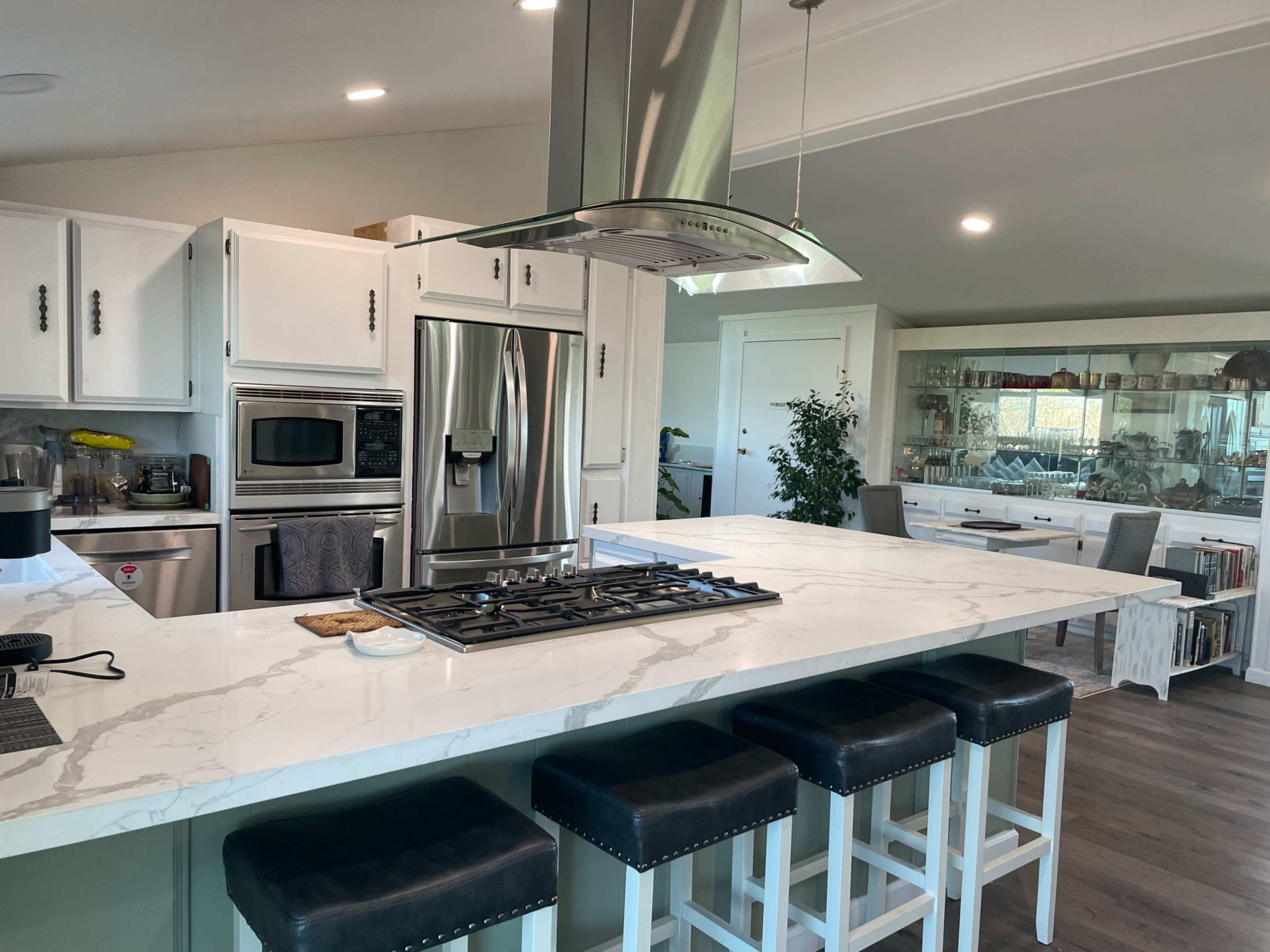 A modern kitchen features a large island with seating, a stainless steel range hood, and sleek white cabinetry.