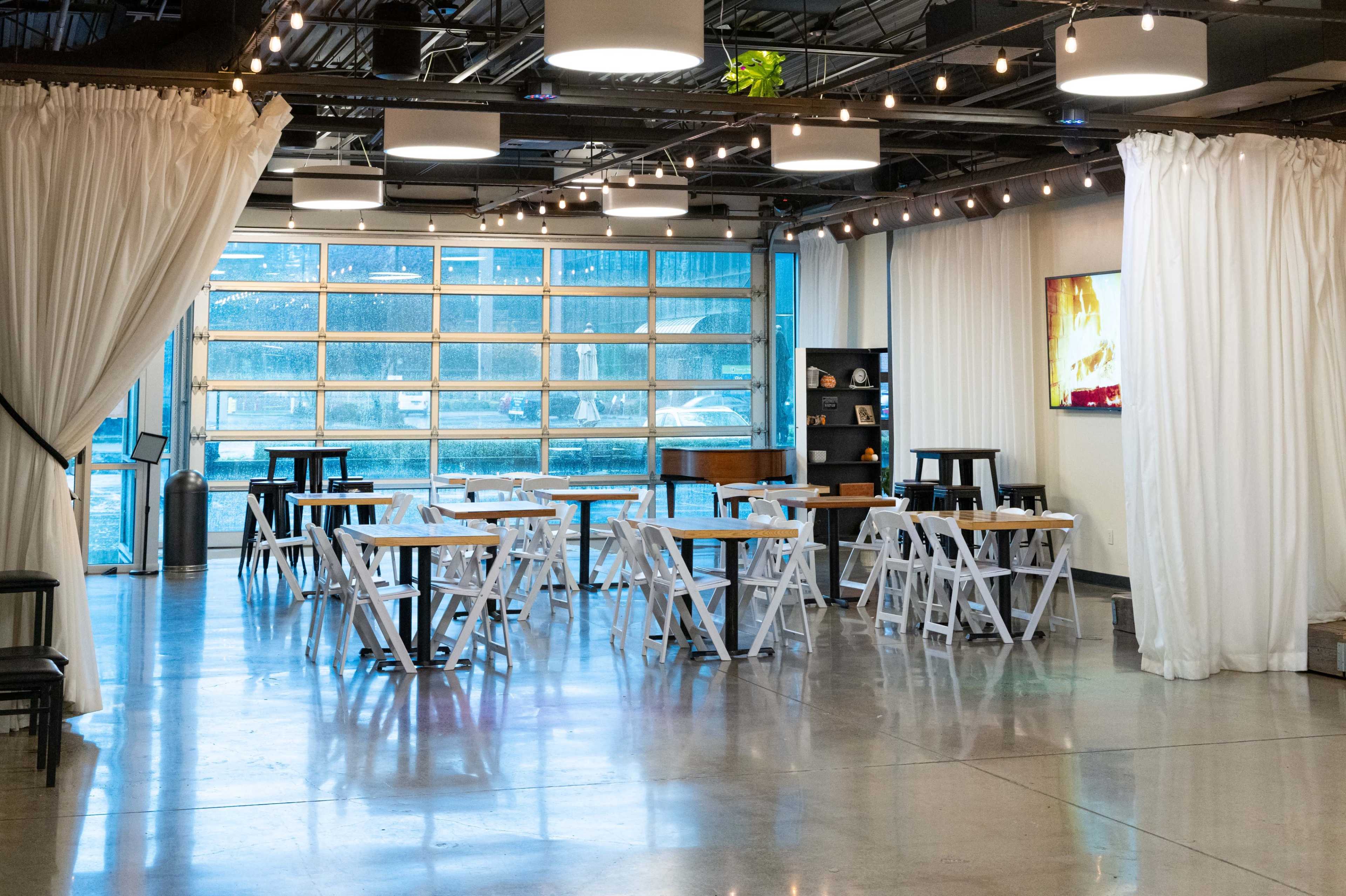 A modern indoor venue with folding tables and chairs, large windows, and soft lighting from overhead fixtures.