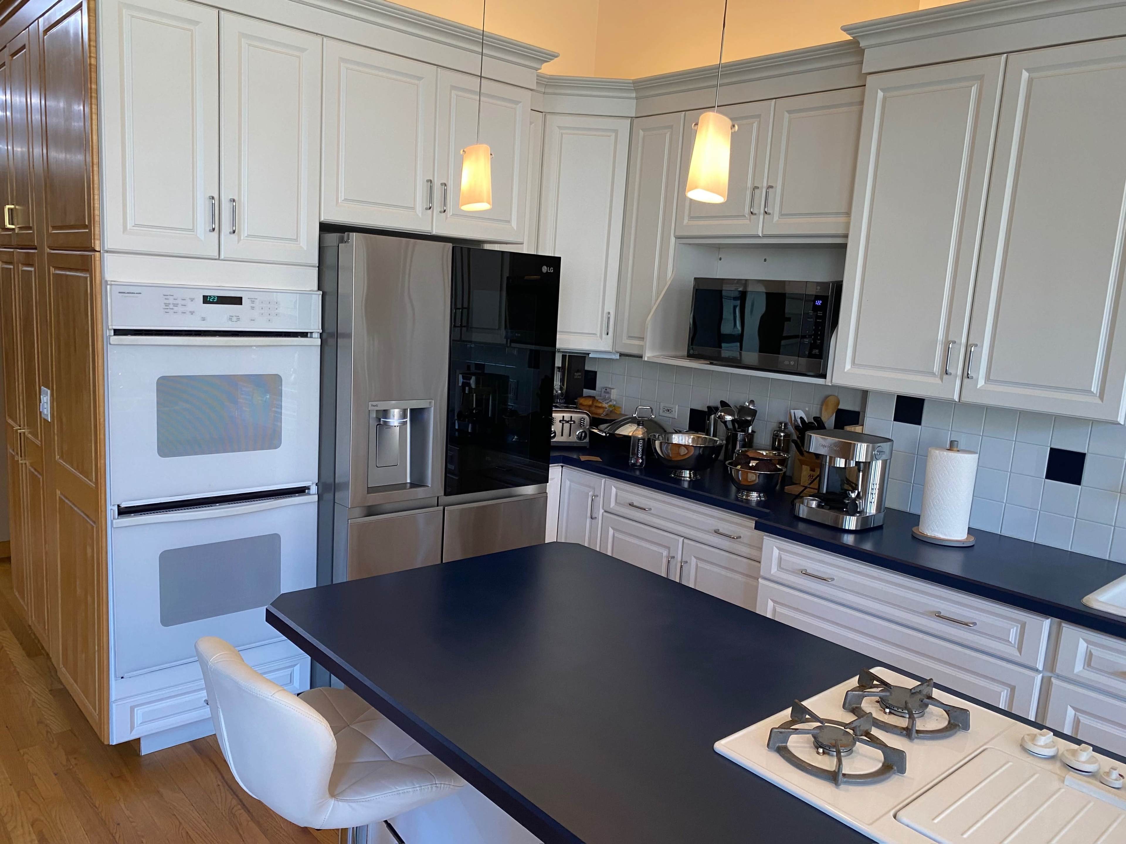 A modern kitchen features white cabinetry, stainless steel appliances, and a dark blue island with a gas stovetop and seating.