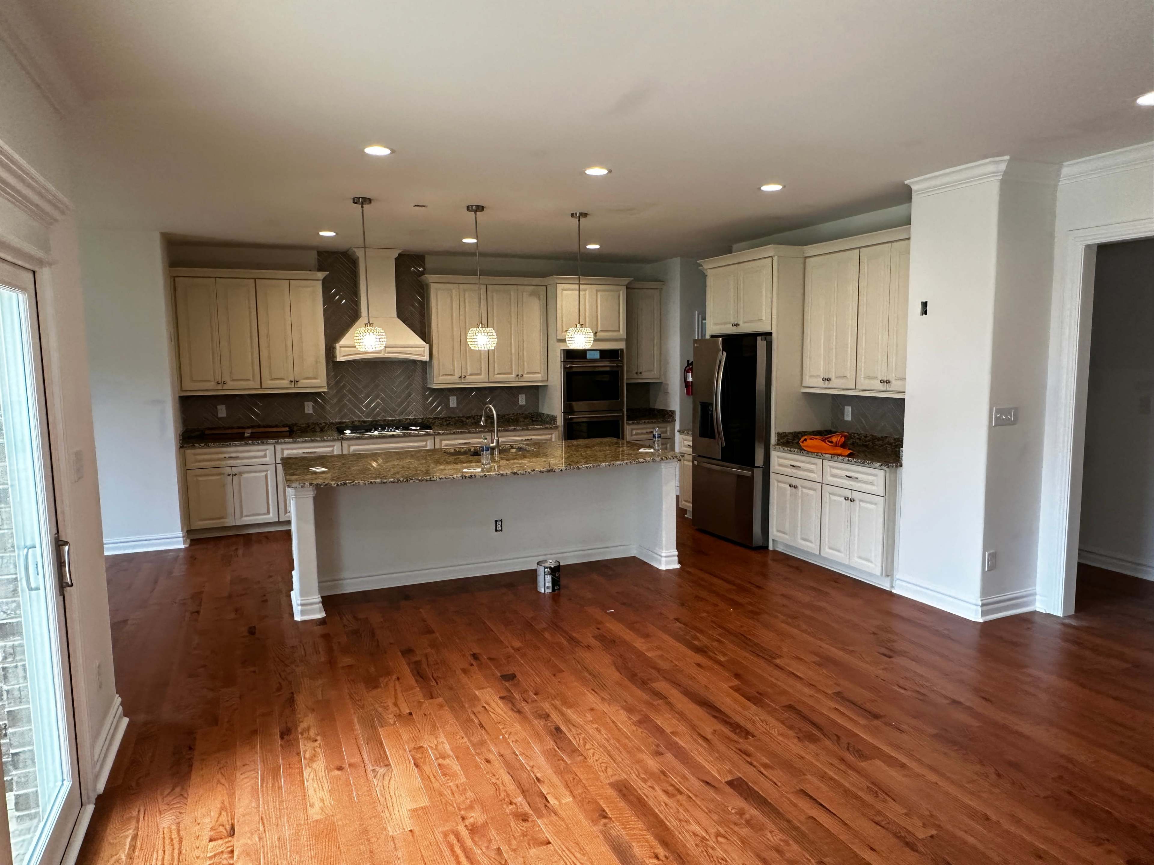 A spacious kitchen with light-colored cabinetry, granite countertops, and hardwood flooring, featuring an island with pendant lighting.
