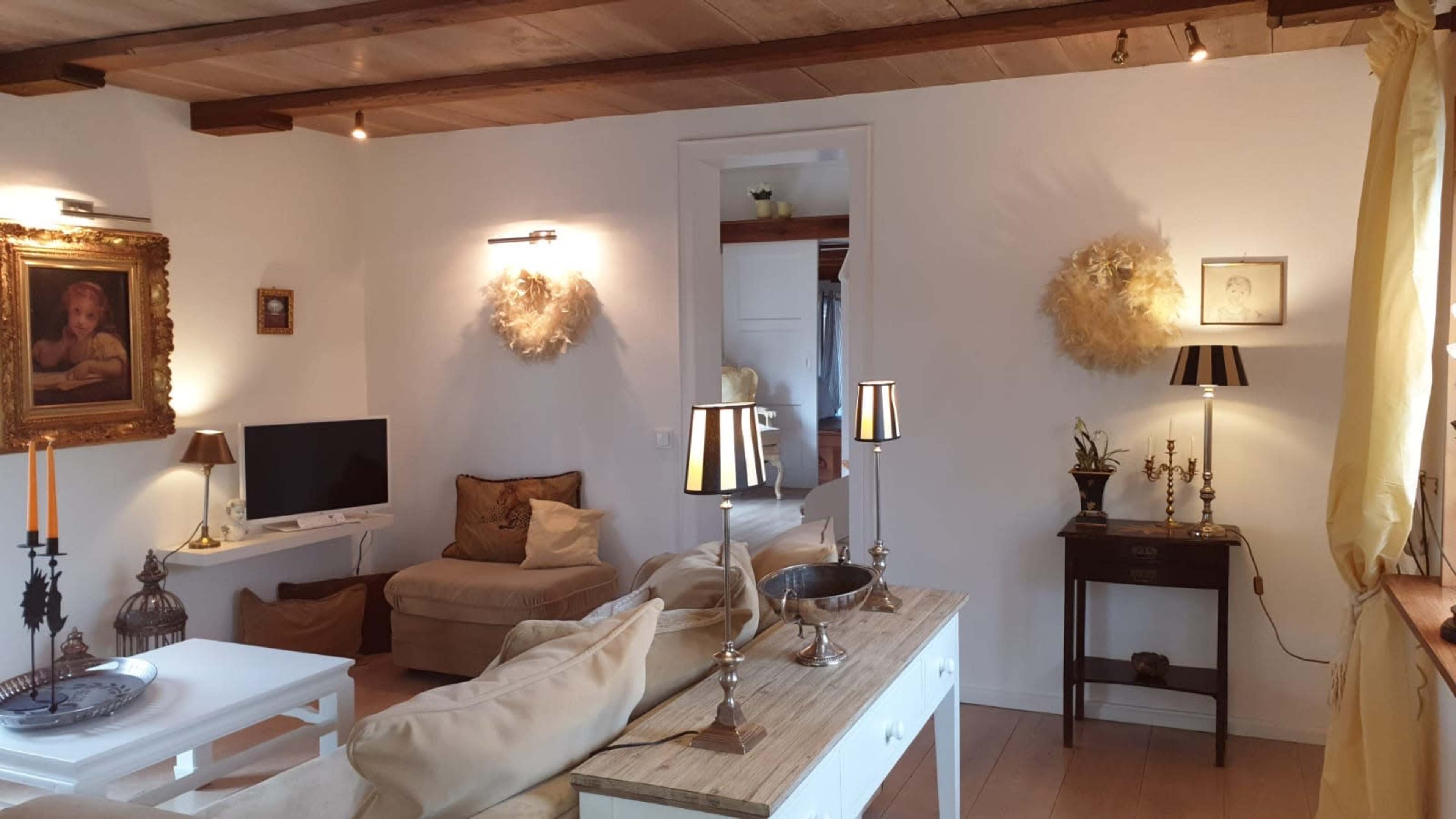 The image shows a tastefully decorated living room featuring a soft-colored sofa, a coffee table, a television, and elegant lighting fixtures.