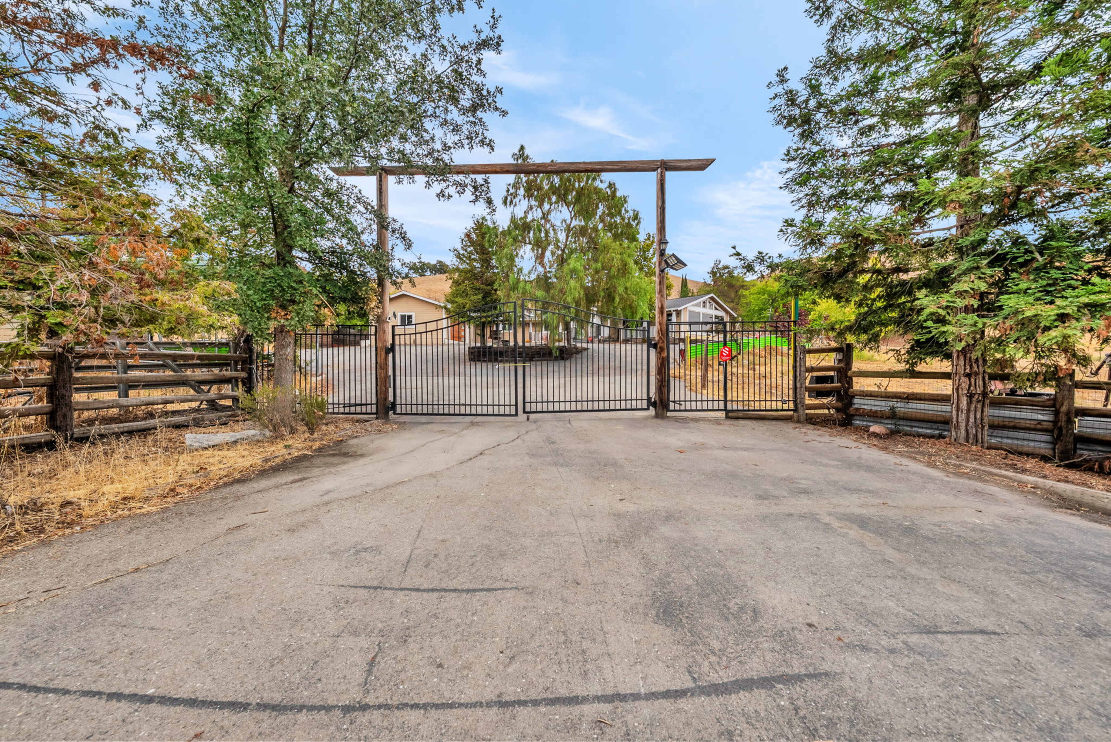 A gated entrance leads to a gravel road surrounded by trees and wooden fencing.